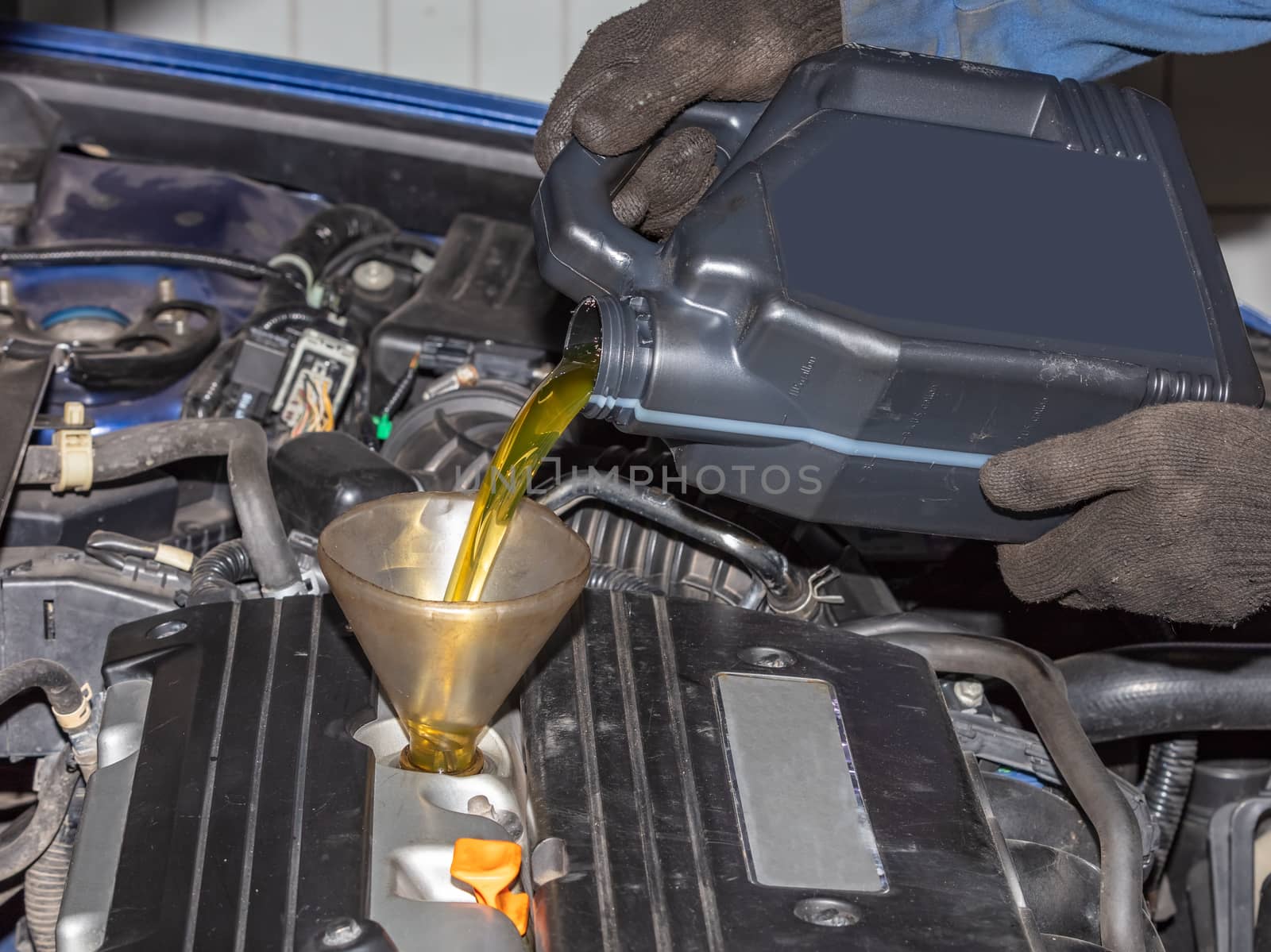 Mechanic topping up the oil in a car pouring a pint of oil through a funnel into the engine, close up of his hands and the oil by DamantisZ