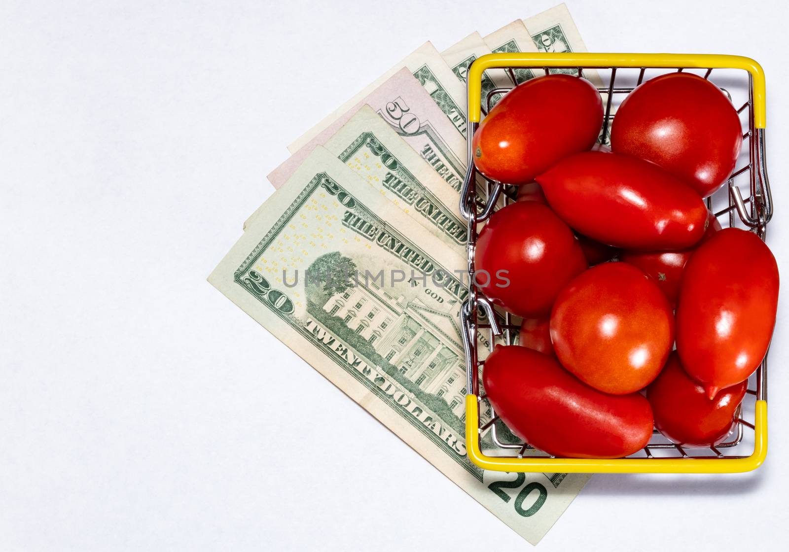 Shot of tomatoes in shopping basket isolated on white background with various US dollar bills underneath it. Ripe tasty red tomatos in shopping basket. Top view. Copy space. by DamantisZ