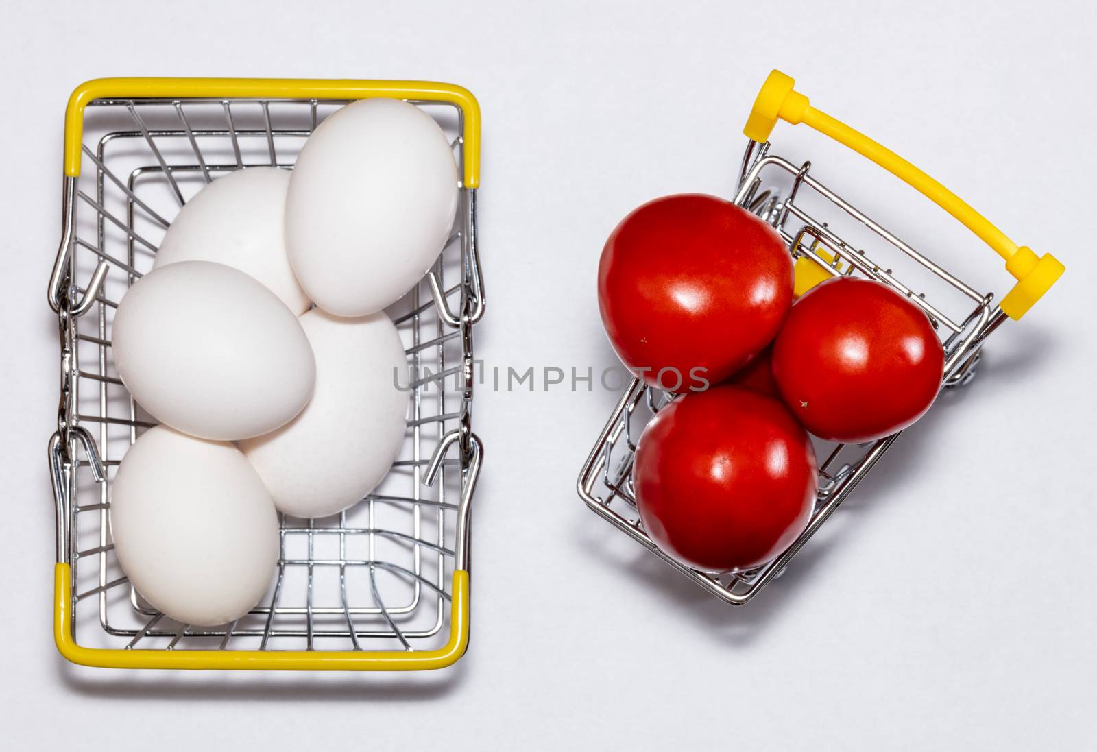 Fresh eggs and tomatoes in a shopping cart and a basket next to it. All mixed up. Top view. Shopping, purchasing, and food delivery concept. White background. Close up shot. Isolated.