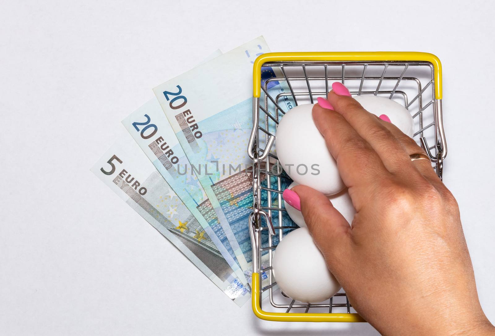 Fresh eggs in a shopping cart with various euro bills underneath it and womans hand reaching for eggs. Shopping, purchasing, and food delivery concept. White background. Close up shot. Isolated.