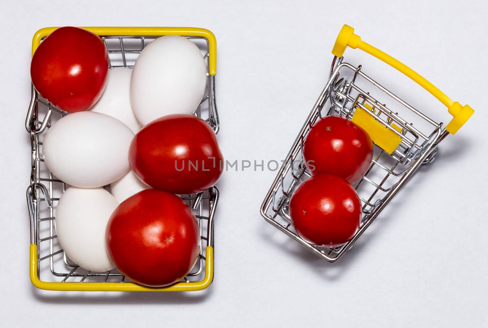 Fresh eggs and tomatoes in a shopping cart and a basket next to it. All mixed up. Top view. Shopping, purchasing, and food delivery concept. by DamantisZ