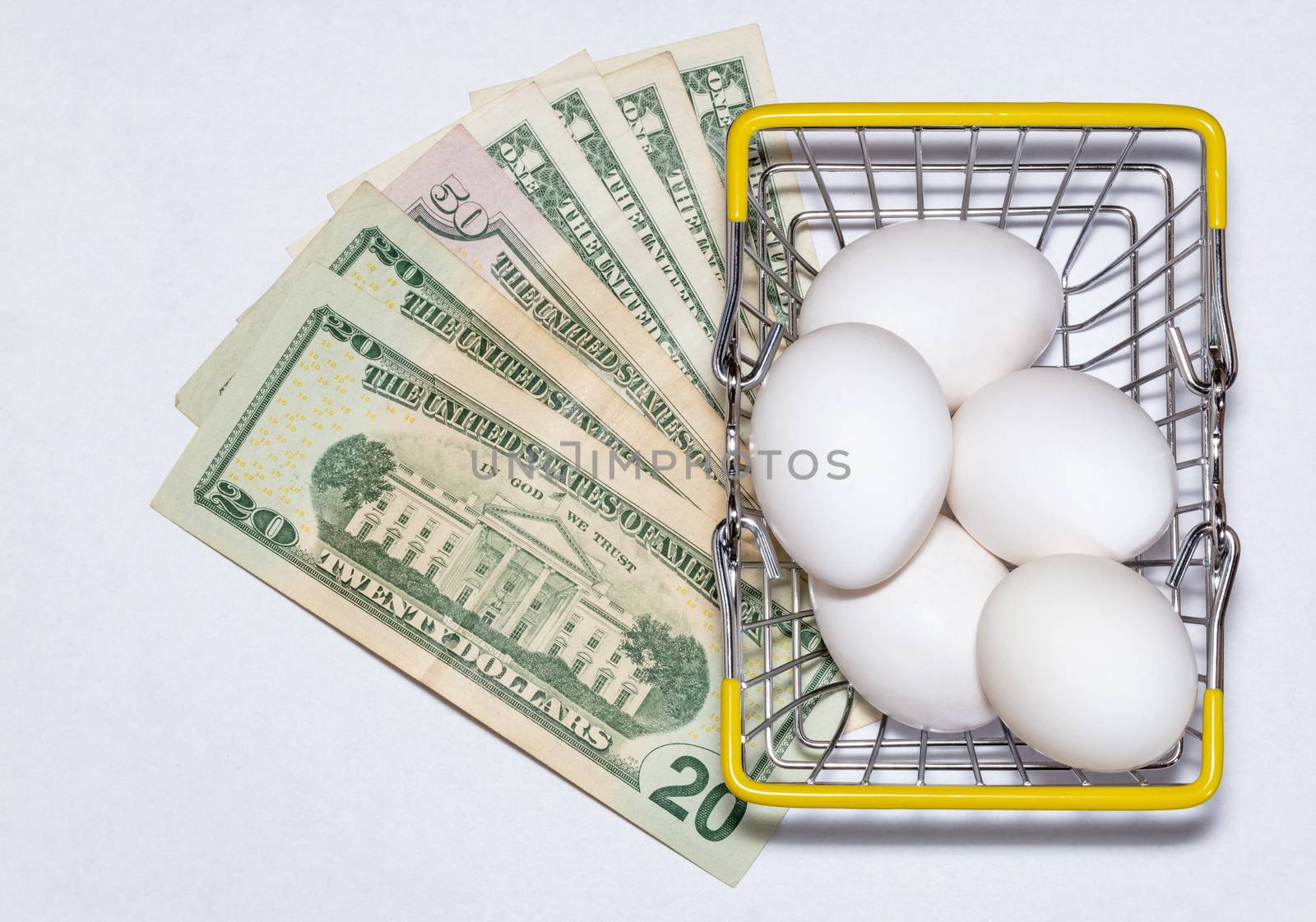 Fresh eggs in a shopping cart with various US dollar bills underneath it. Shopping, purchasing, and food delivery concept. White background. Close up shot. Isolated.