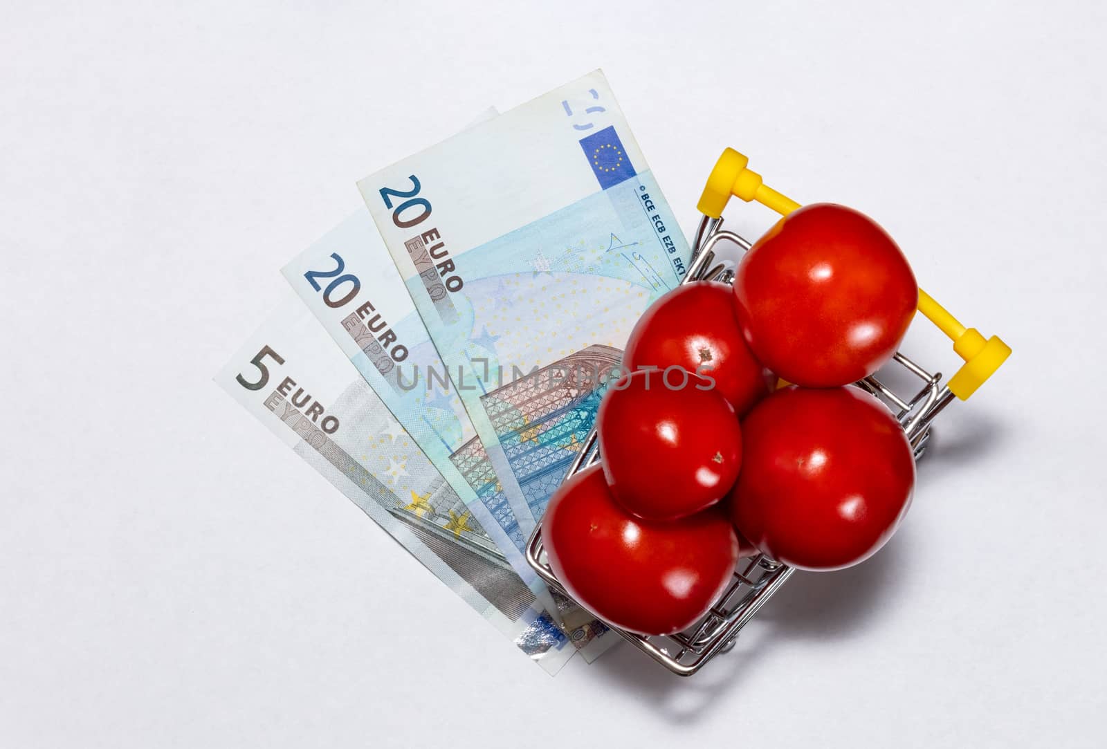 Shot of tomatoes in shopping cart isolated on white background with euro bills under it. Top view. Ripe tasty red tomatos in shopping cart. Tomato trading concept. Online shopping concept.