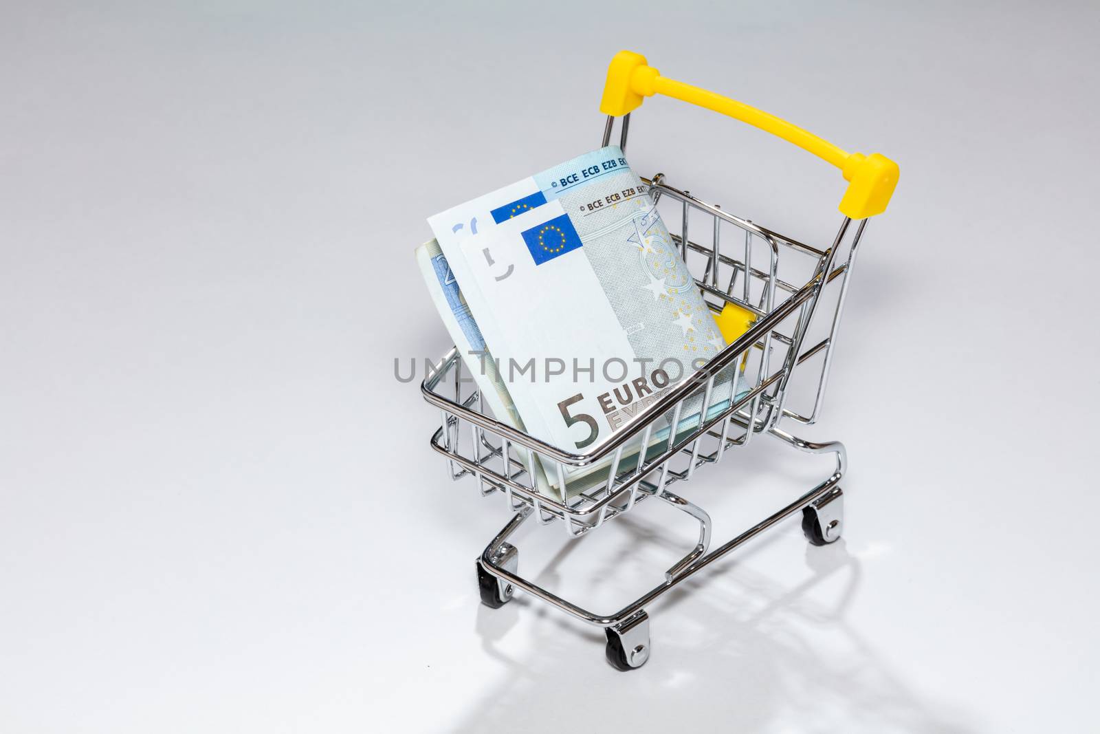 High angle shot of a cart from the supermarket with money. Euro on a white background. Concept of purchasing cost, a trip to the supermarket, costs of everyday shopping, expenses