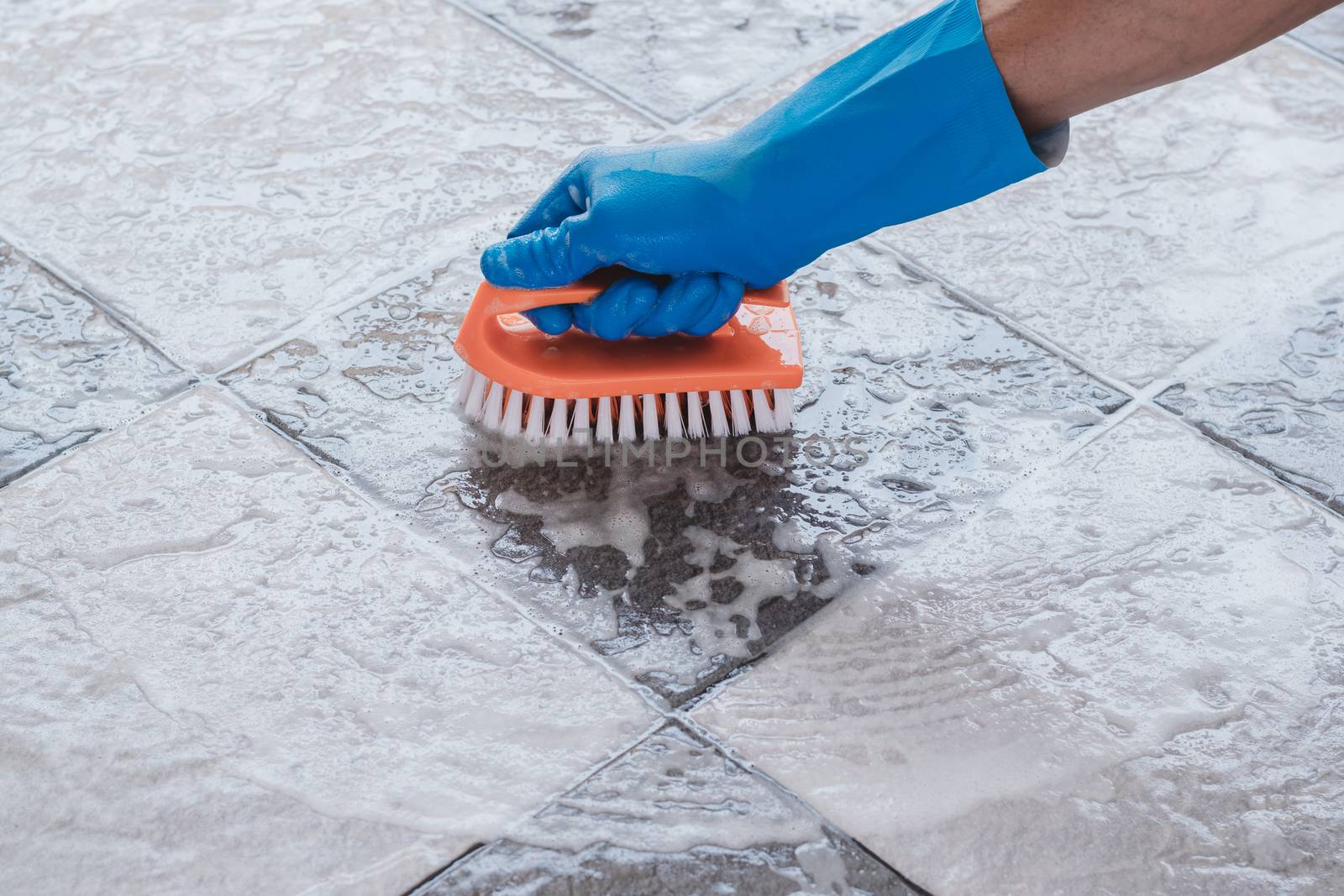 Hand of man wearing blue rubber gloves is used to convert scrub cleaning on the tile floor.