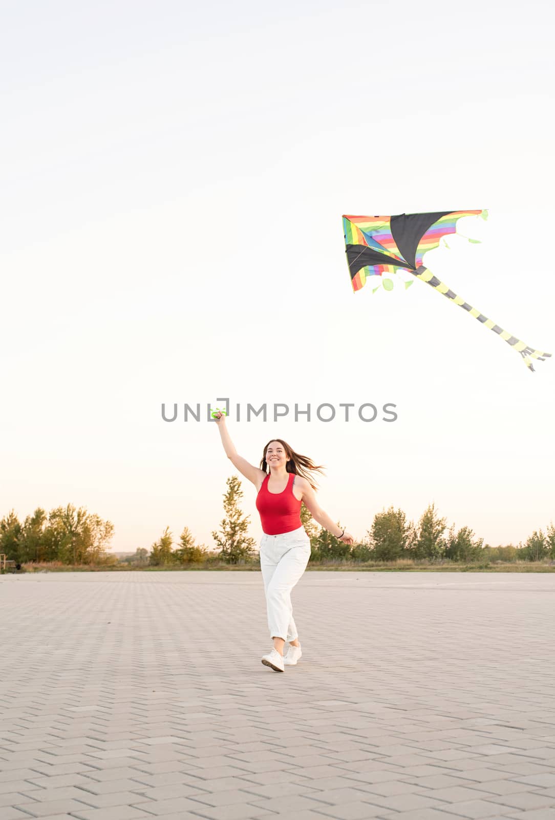 Young woman flying a kite in a public park at sunset by Desperada