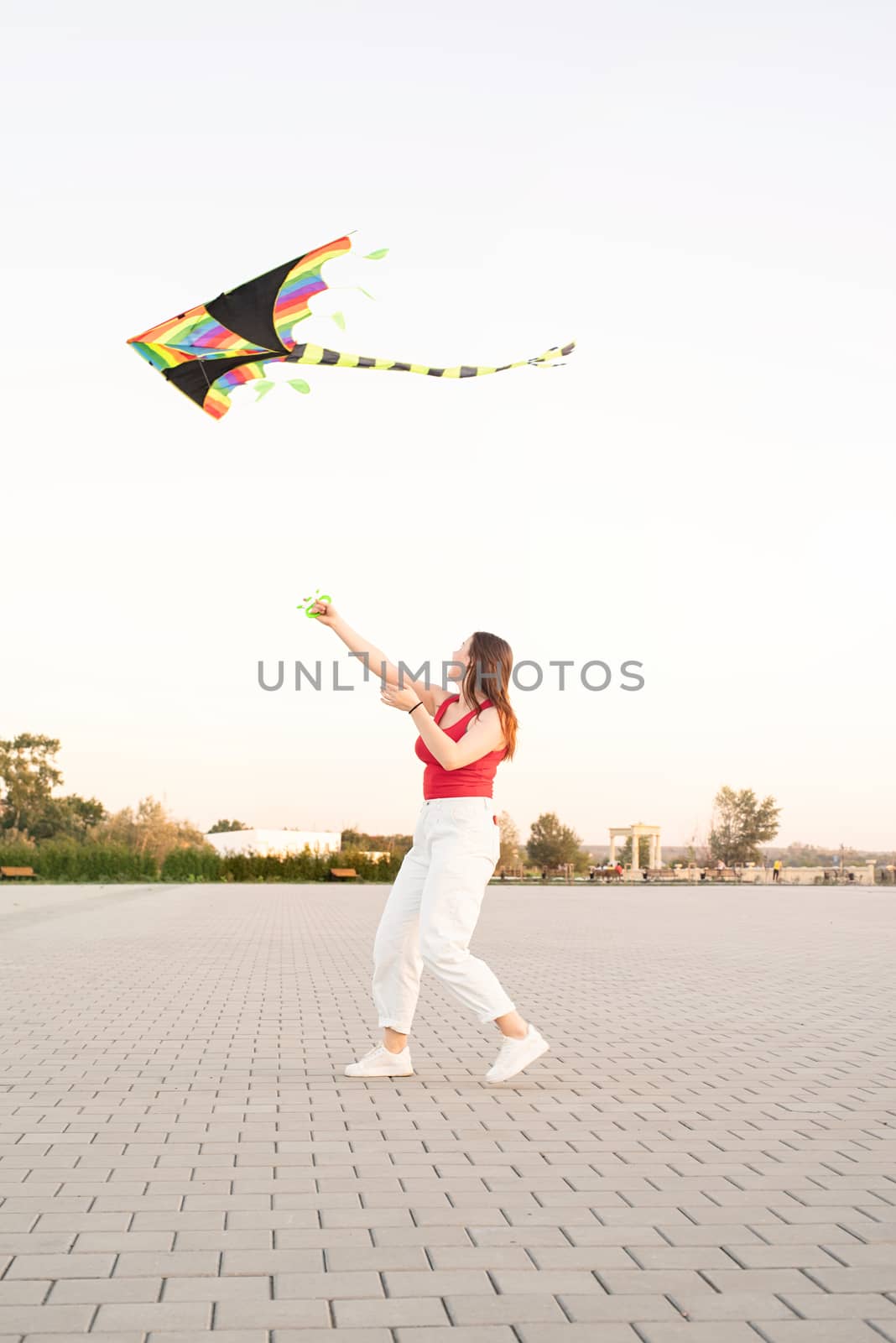 Young woman flying a kite in a public park at sunset by Desperada