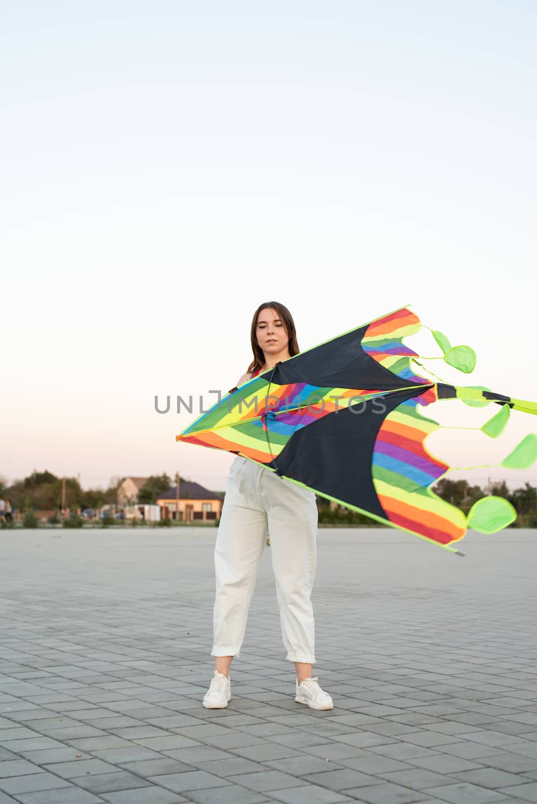 Young woman flying a kite in a public park at sunset by Desperada