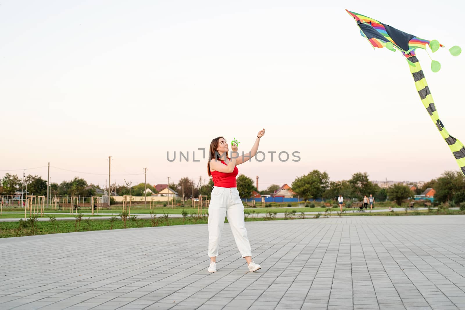 Young woman flying a kite in a public park at sunset by Desperada