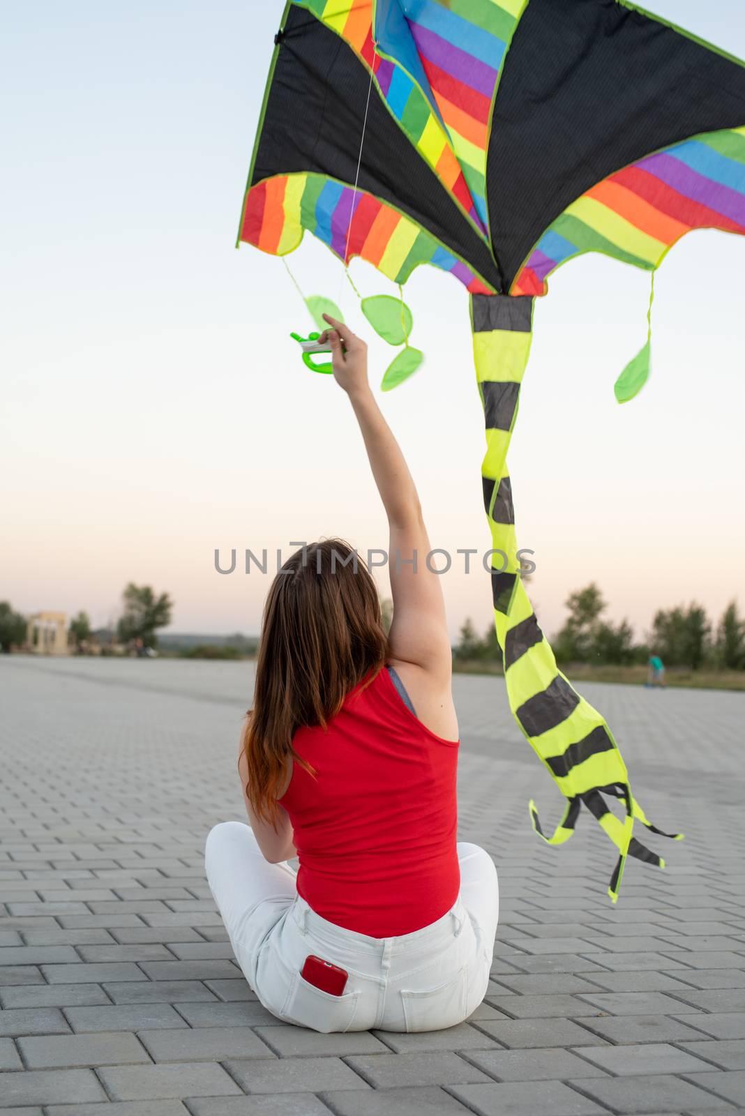 Young woman flying a kite in a public park at sunset by Desperada