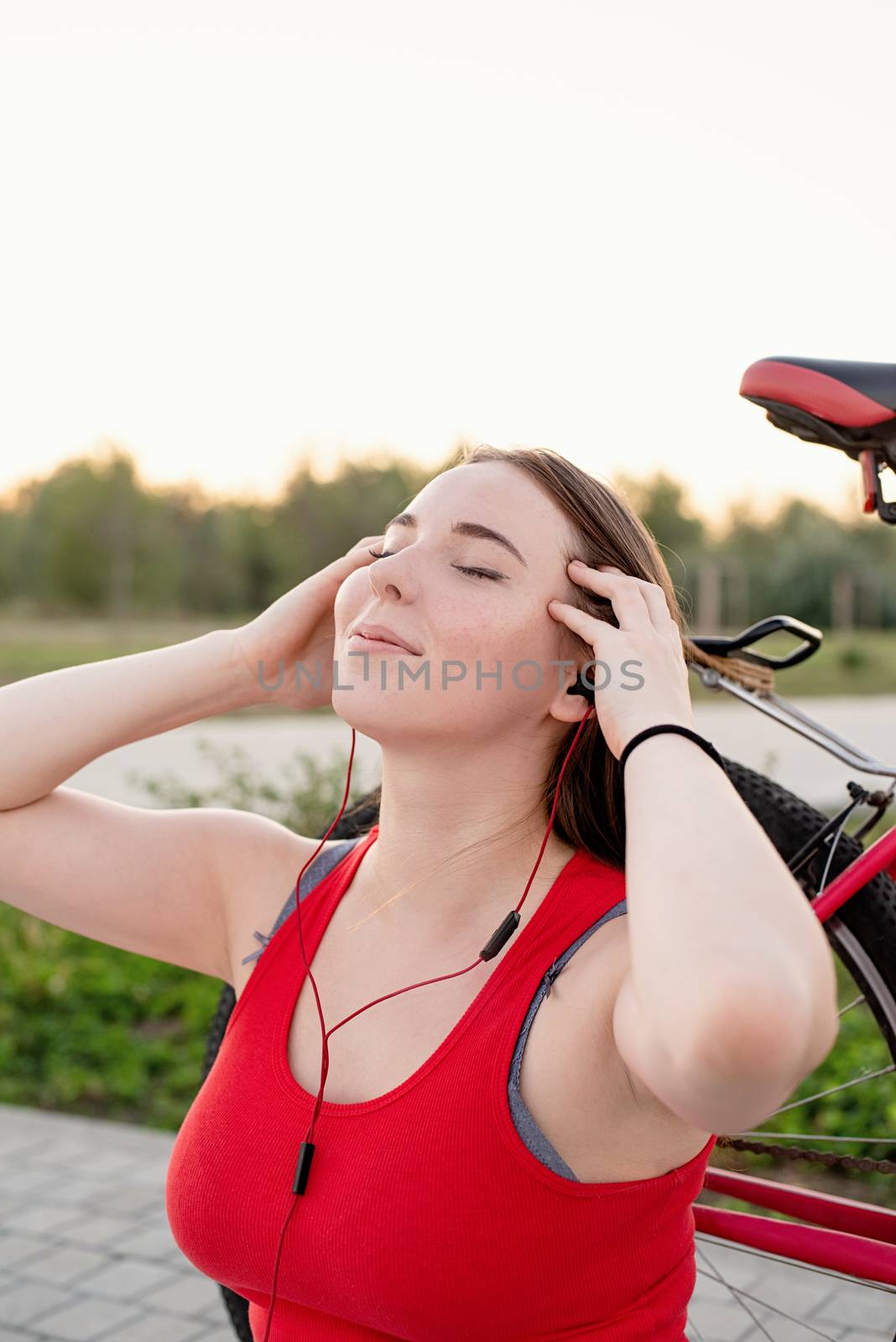 Teenage girl sitting next to her bike listening to the music in the park