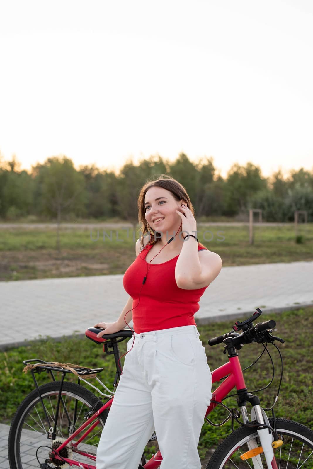 Teenage girl with her bike listening to the music in the park at sunset by Desperada