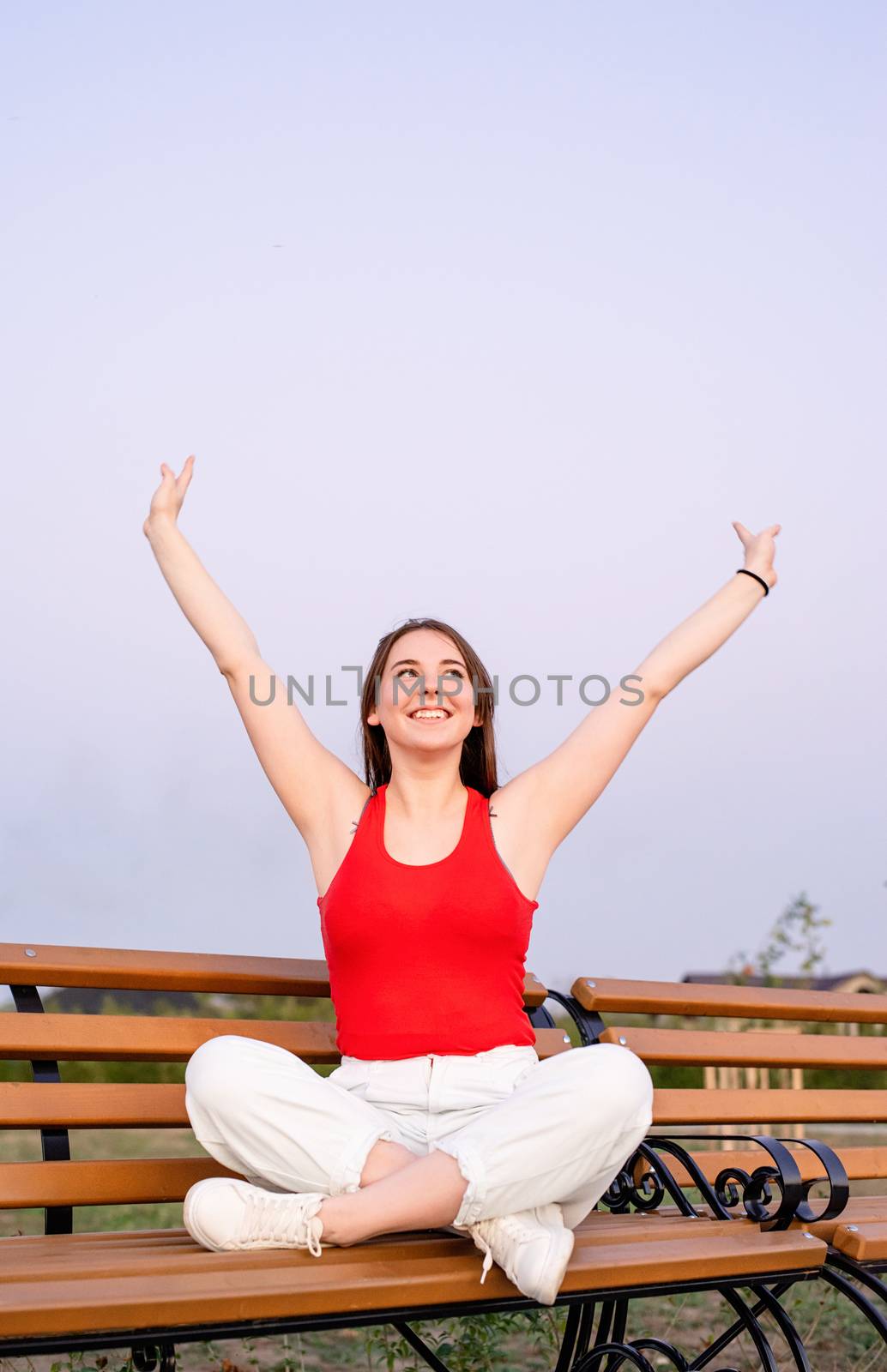 Happy young woman sitting on a bench with crossed legs by Desperada