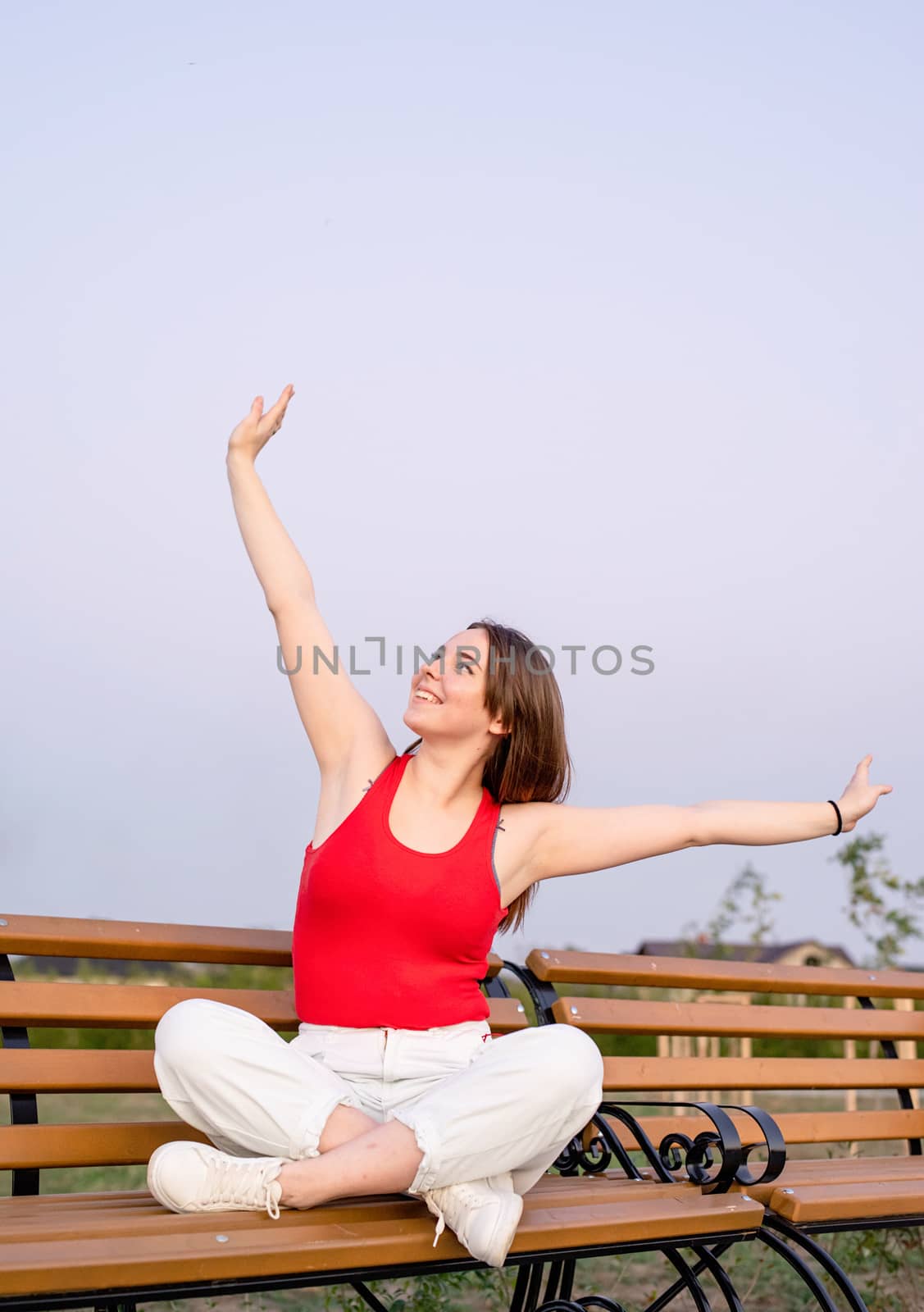 Happy young woman sitting on a bench with crossed legs by Desperada