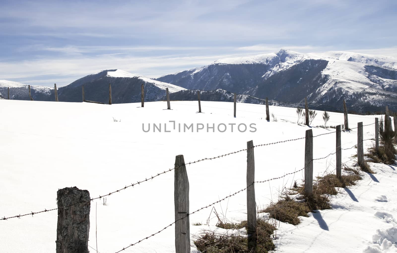 Snowy landscape with a fence in the foreground and mountains in the background. Copy space.
