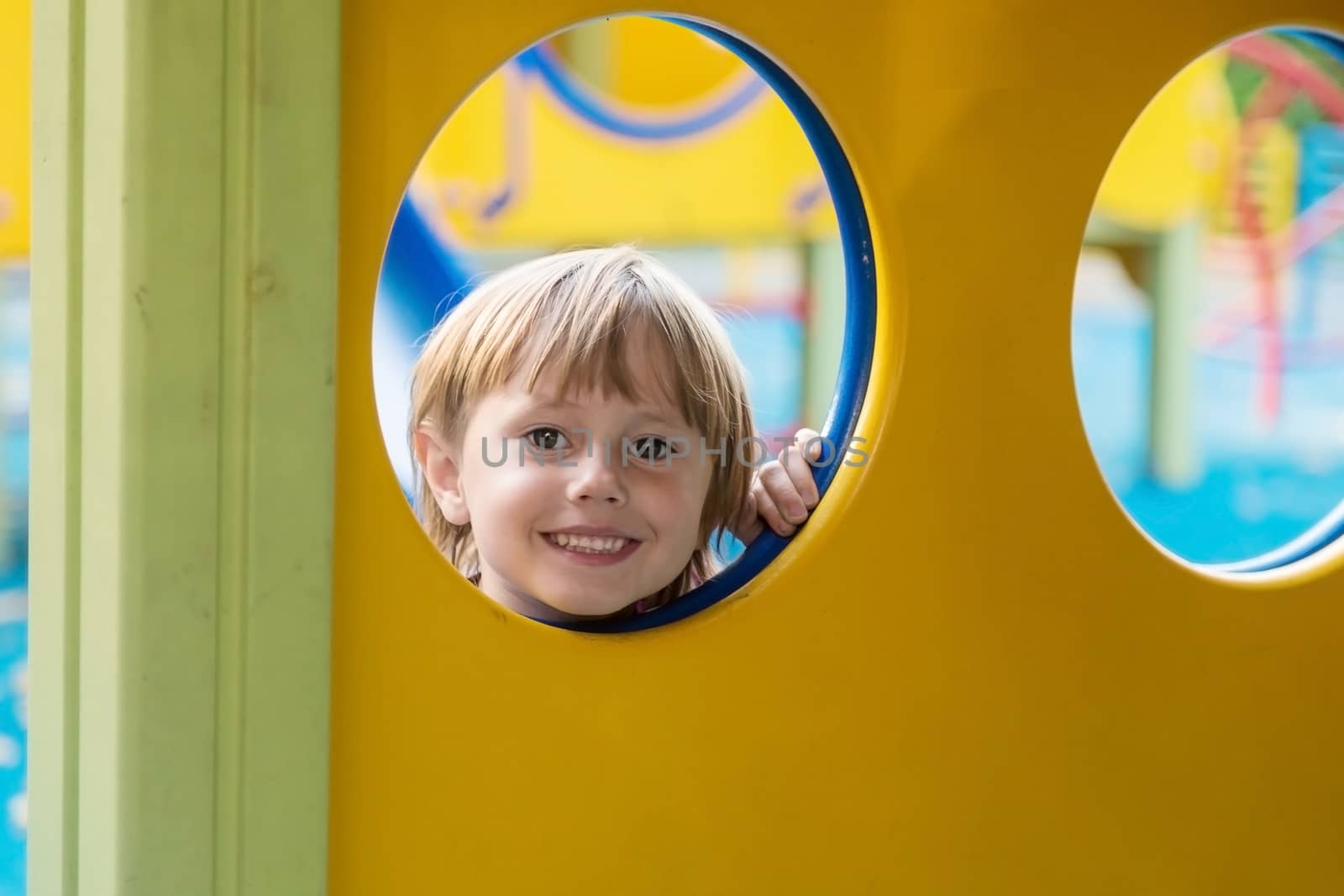 The girl looks out from the circle of the slide on the playground looks at the camera and smiles.