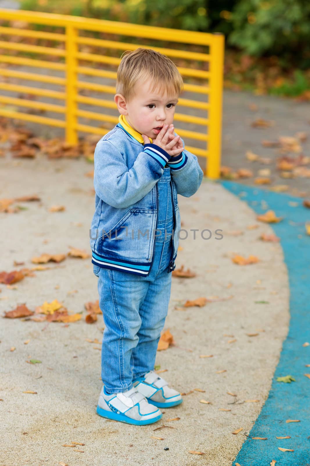 .A little boy in denim clothes stands scared alone in the middle of a playground in an autumn park.