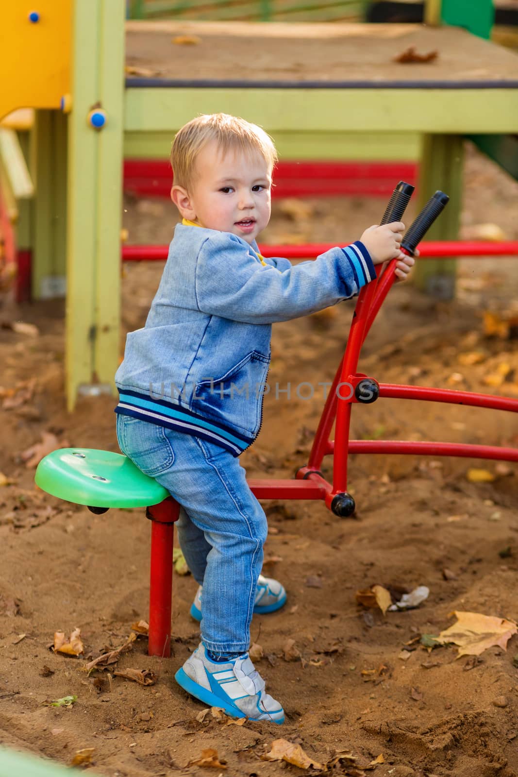 Little boy plays with a toy excavator on the playground in the autumn park. by galinasharapova