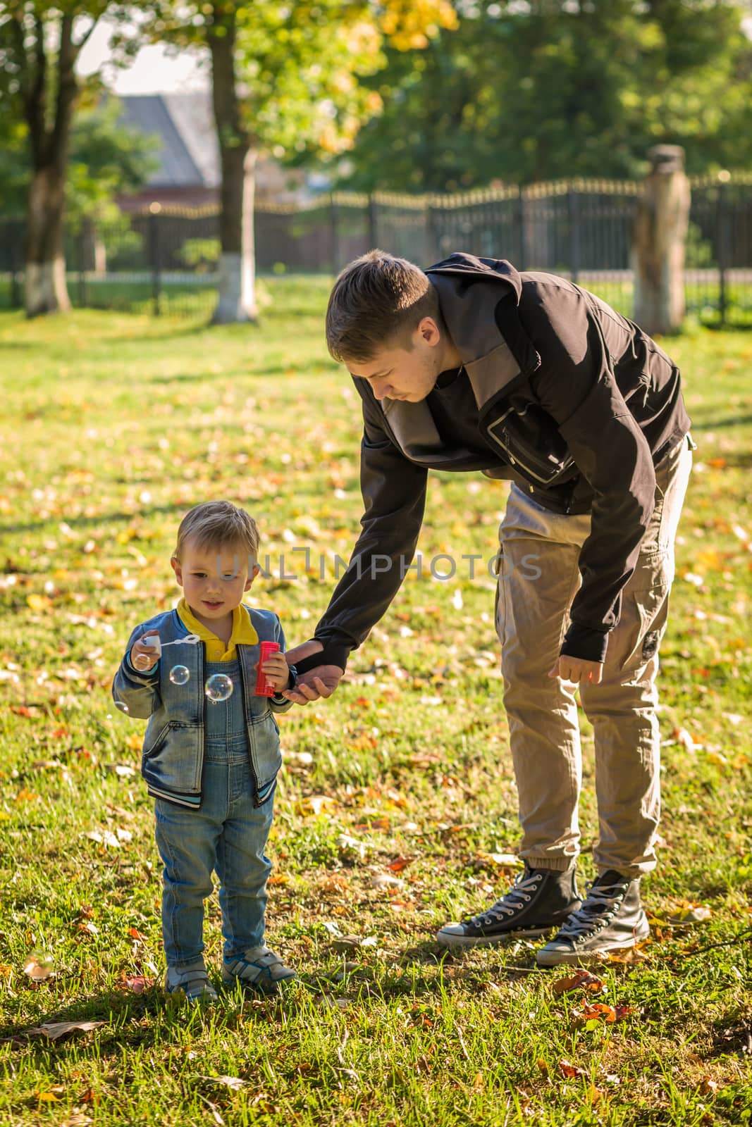 .Dad helps his son to blow bubbles in an autumn park. by galinasharapova
