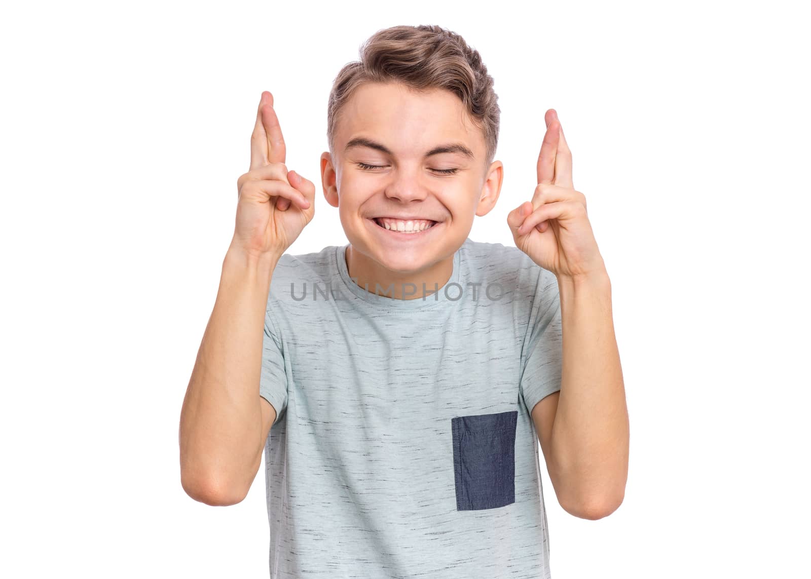 Portrait of teen boy crossing his fingers and wishing for good luck, isolated on white background. Caucasian teenager praying with crossed fingers and eyes closed. Child face expression emotions.
