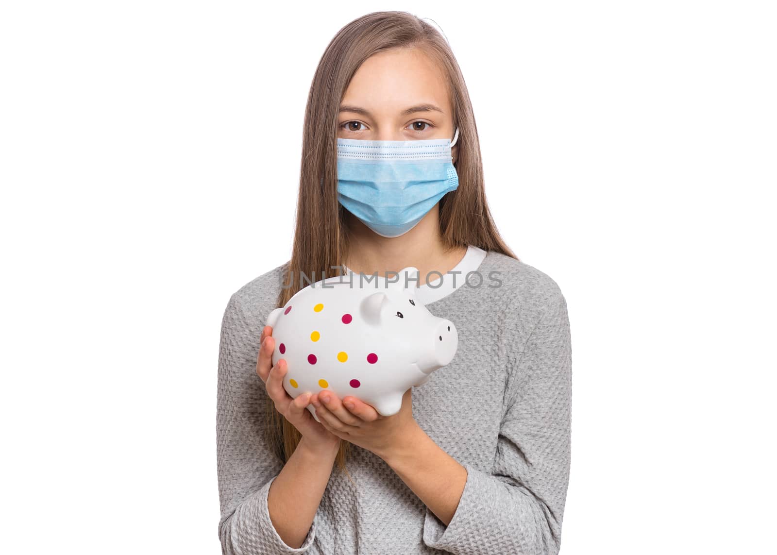 Concept of coronavirus quarantine. Portrait of teen girl wearing medical protective mask. Child holding Piggy Bank. Saving Money concept. COVID-19.