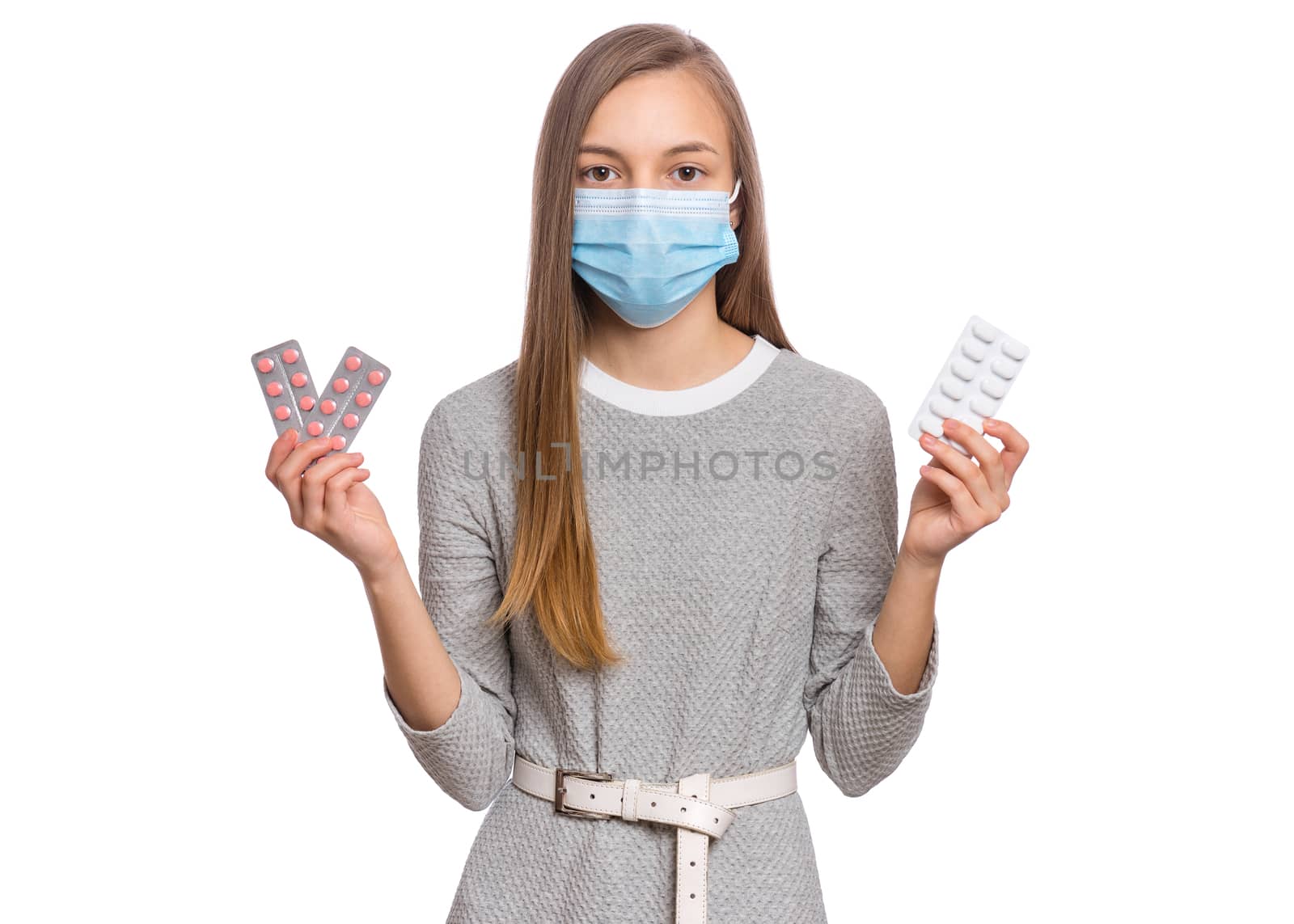 Concept of coronavirus. COVID-19. Child wearing medical face mask - protection from influenza virus, on white background. Teen girl holds pills.