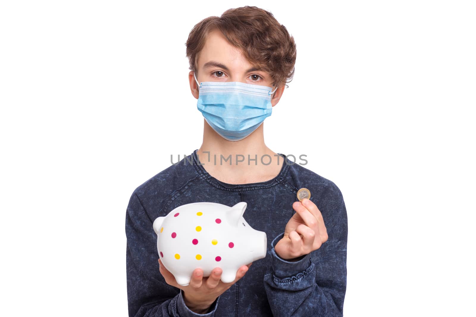 Concept of coronavirus quarantine. Portrait of teen boy wearing medical protective mask. Child holding Piggy Bank and coin. Saving Money concept. COVID-19 - home self isolation.