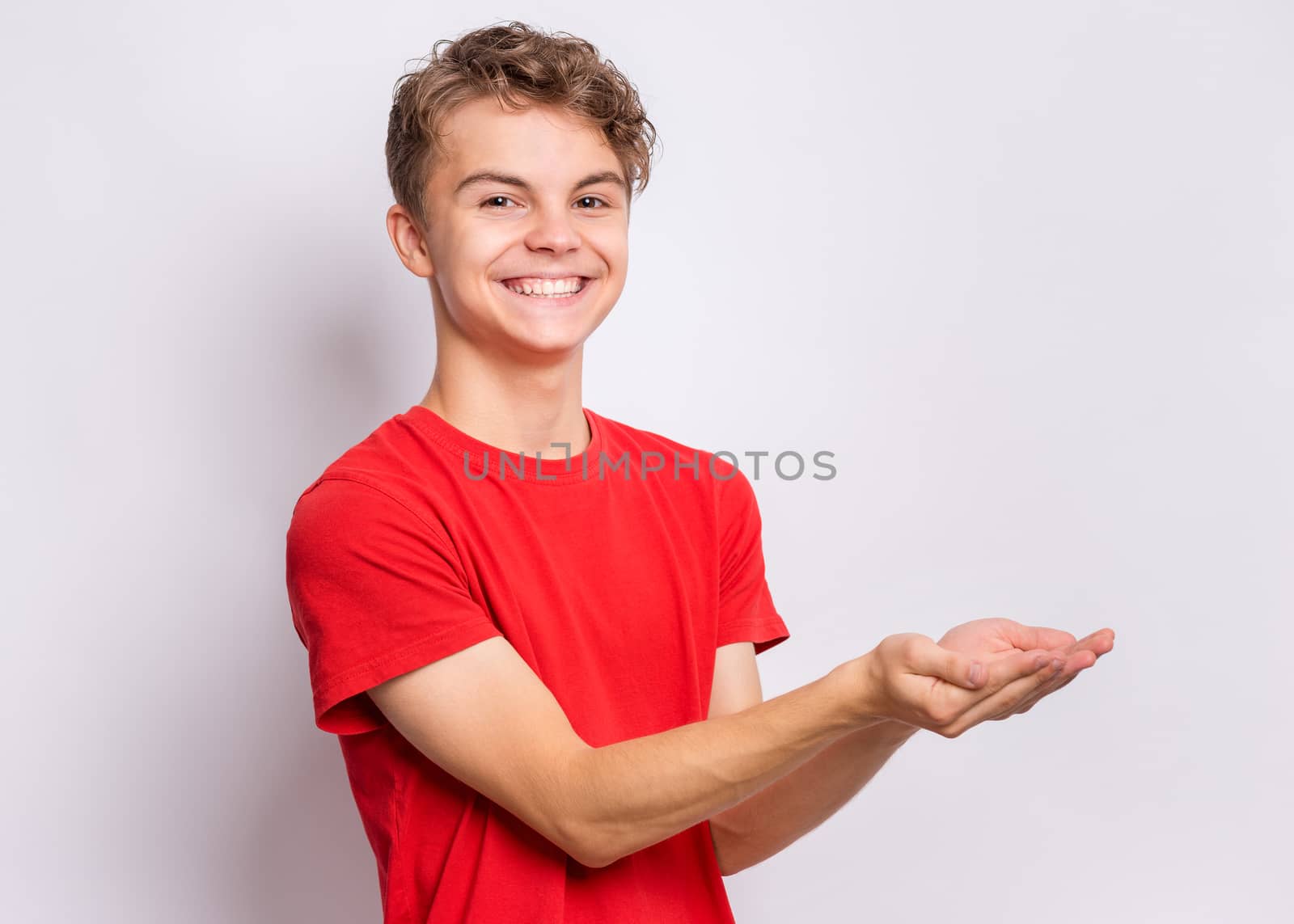 Portrait of cute smiling teen boy holding nothing - side view. Happy teenager with empty palms up - profile, over grey background. Child stretched out his hands - sign of begging or giving.