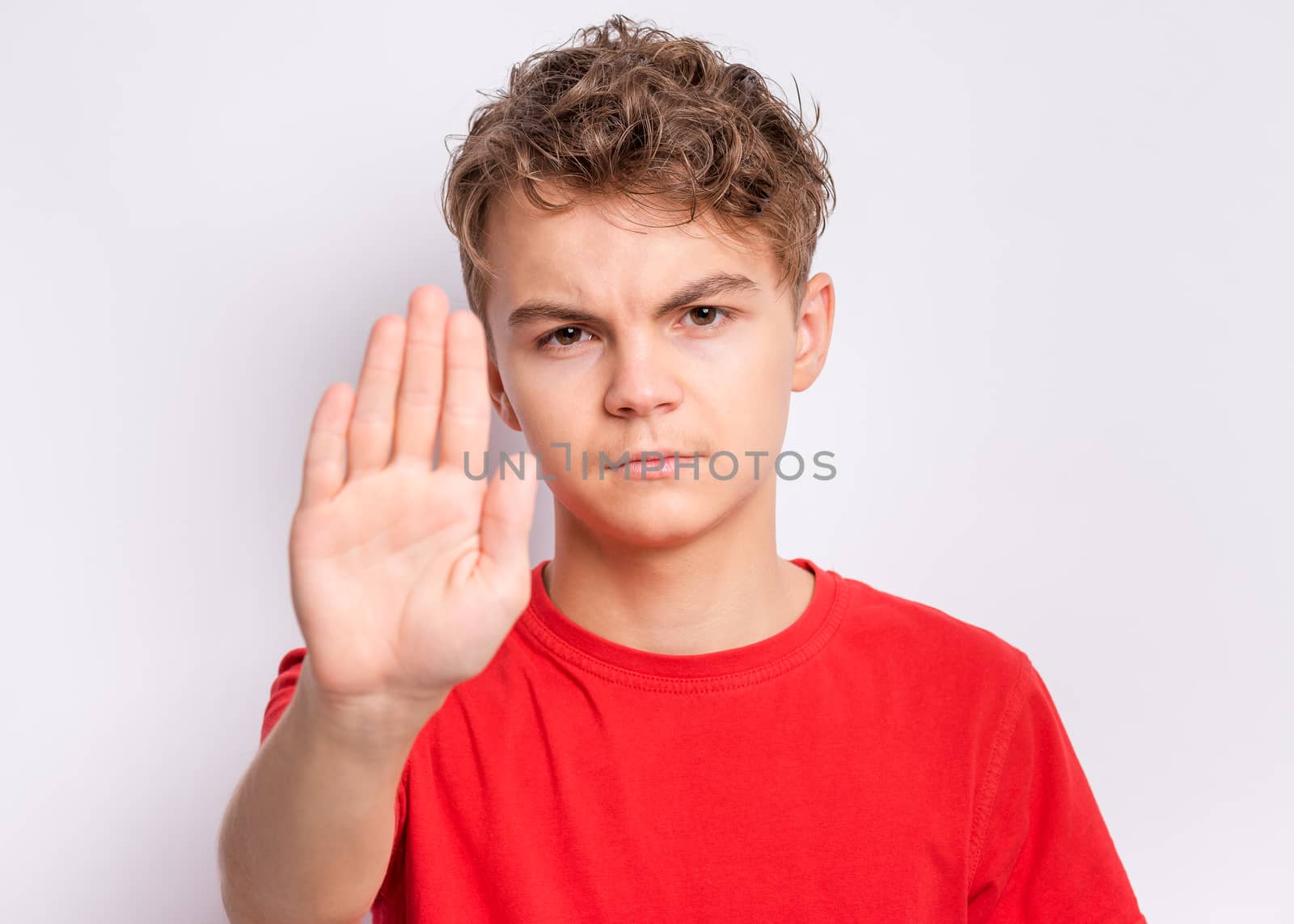 Teen boy doing stop sign with palm of hands, on gray background. Beautiful caucasian teenager making stop gesture.