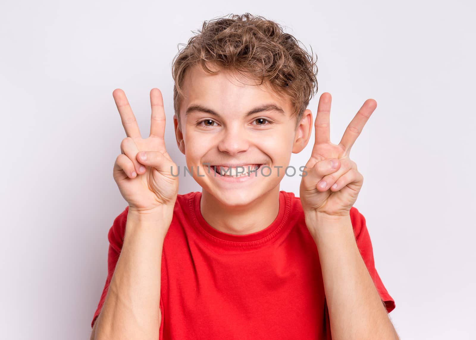 Portrait of teen boy making Victory gesture, on grey background. Handsome caucasian young teenager smiling and showing victory sign. Happy cute child doing victory symbol.