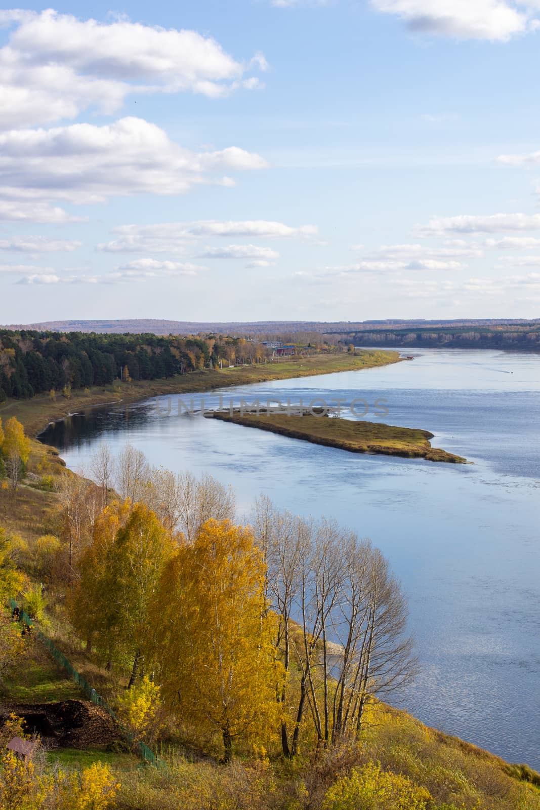 Beautiful, wide river autumn among the woods. Calm and quiet place with autumn colors. In the middle of the river island. View from the top to the distance