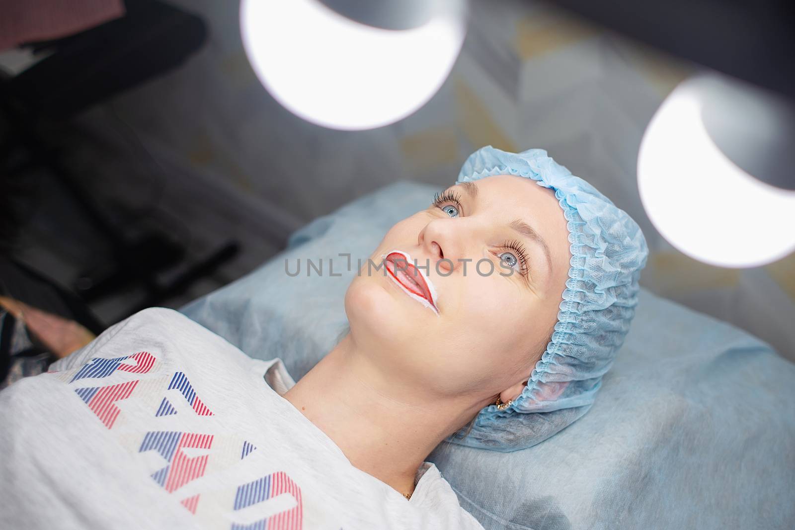 A woman is lying on a table in the office of a permanent make-up master, her lips are anesthetized. Preparation for permanent lip makeup