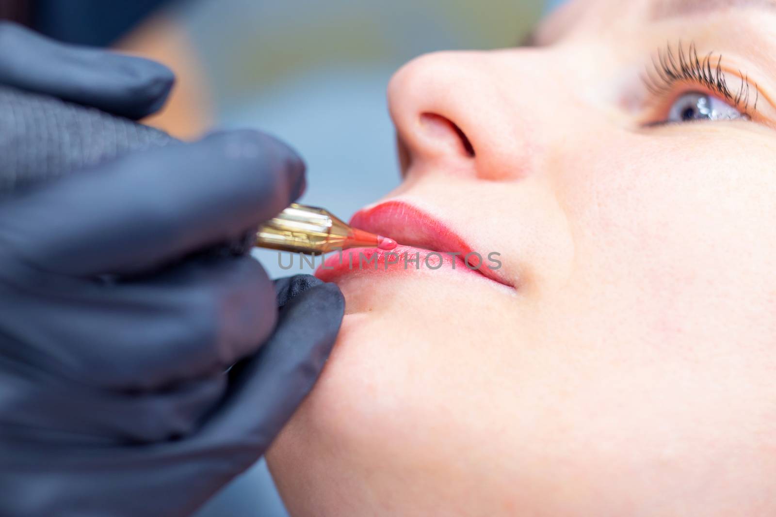The process of applying permanent makeup on the lips with a tattoo machine close-up. Permanent apparatus needle