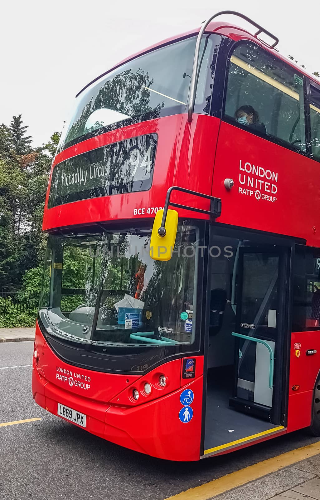 London, UK - July 8, 2020: Modern red double-decker bus is waiting for people in central London. It says on it - Piccadilly Circus 94. A person sitting on the second deck and wearing a mask.