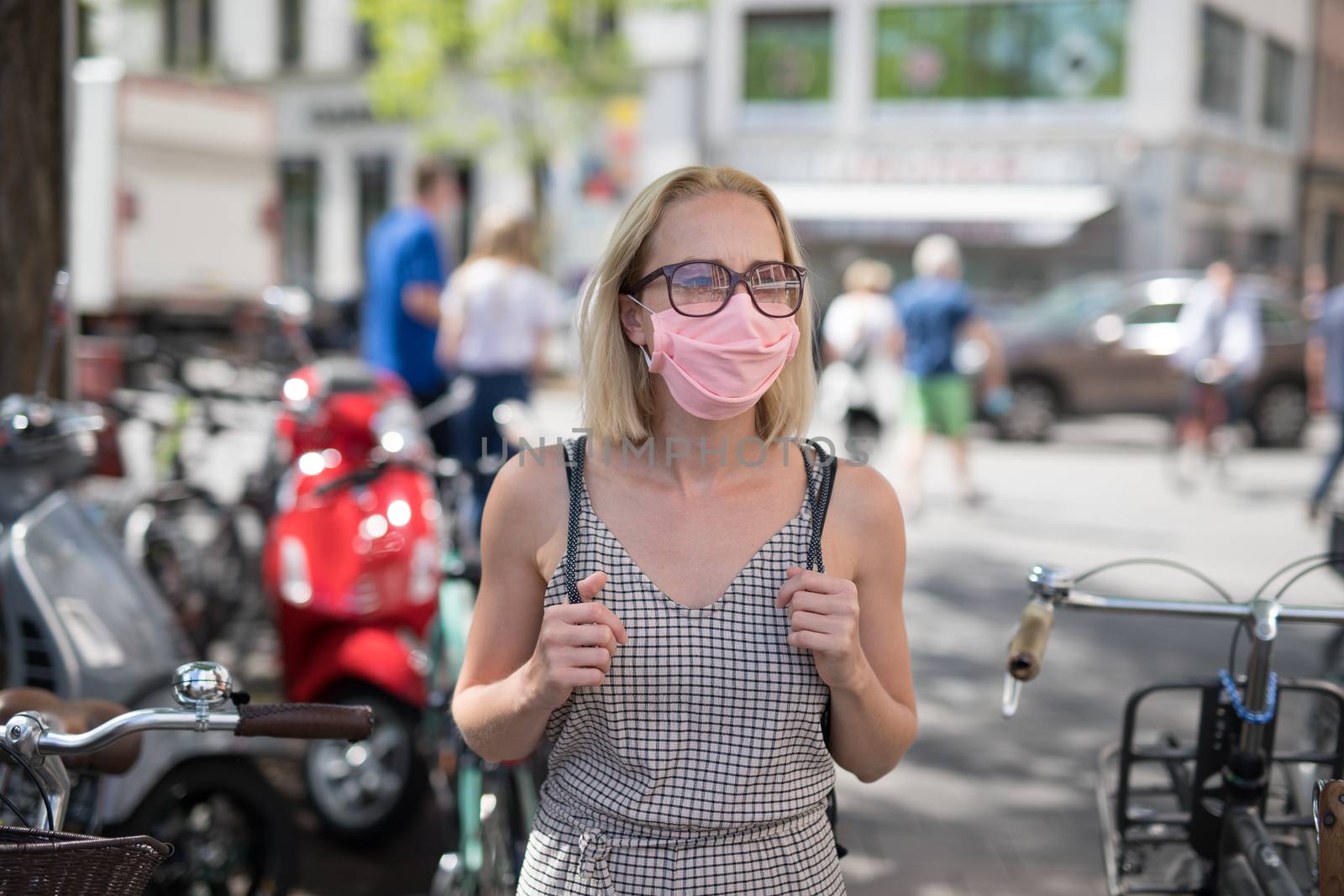 Portrait of casual yound woman walking on the street wearing protective mask as protection against covid-19 virus. Incidental people on the background by kasto