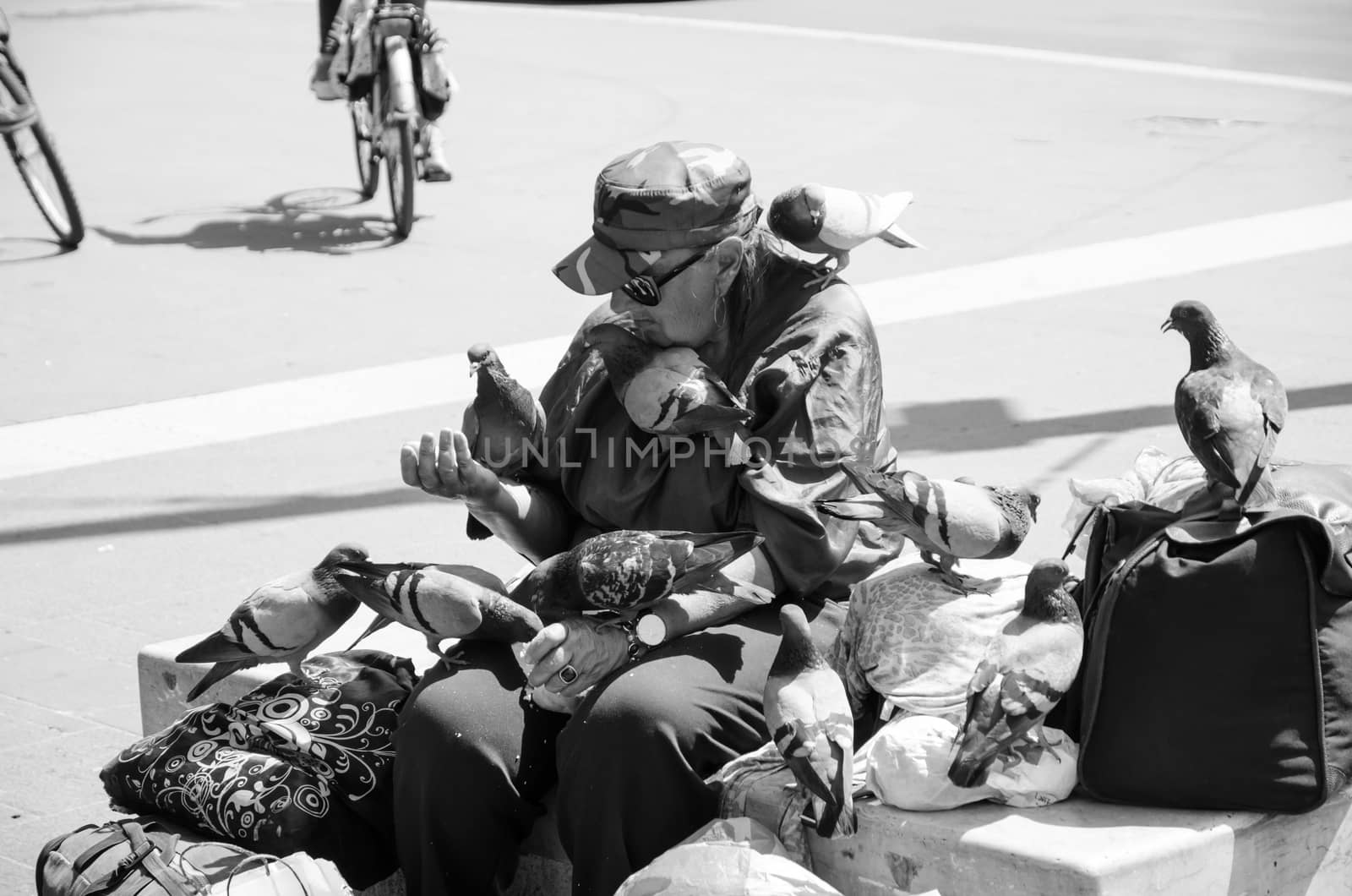 Rome, Italy. April 2019. Pigeons cover a homeless woman intent on feeding them. Black and white picture by cromam70