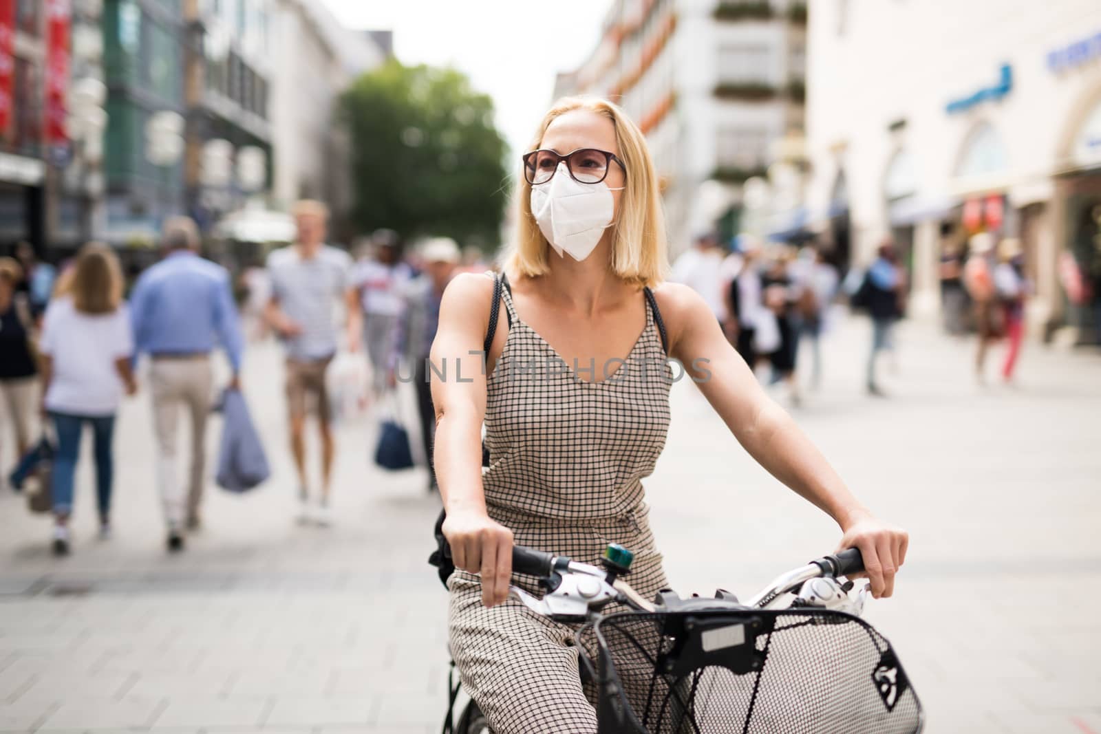 Woman riding bicycle on city street wearing medical face mask in public to prevent spreading of corona virus. New normal during covid epidemic. Social responsibility.