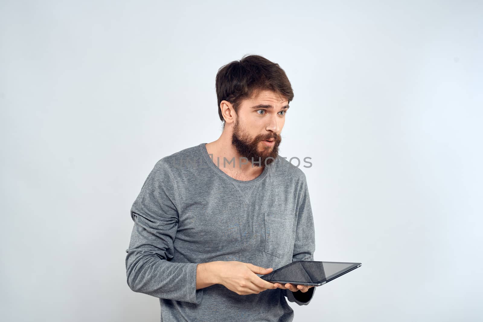 A bearded man with a tablet in his hands a gray jacket technology internet light background. High quality photo