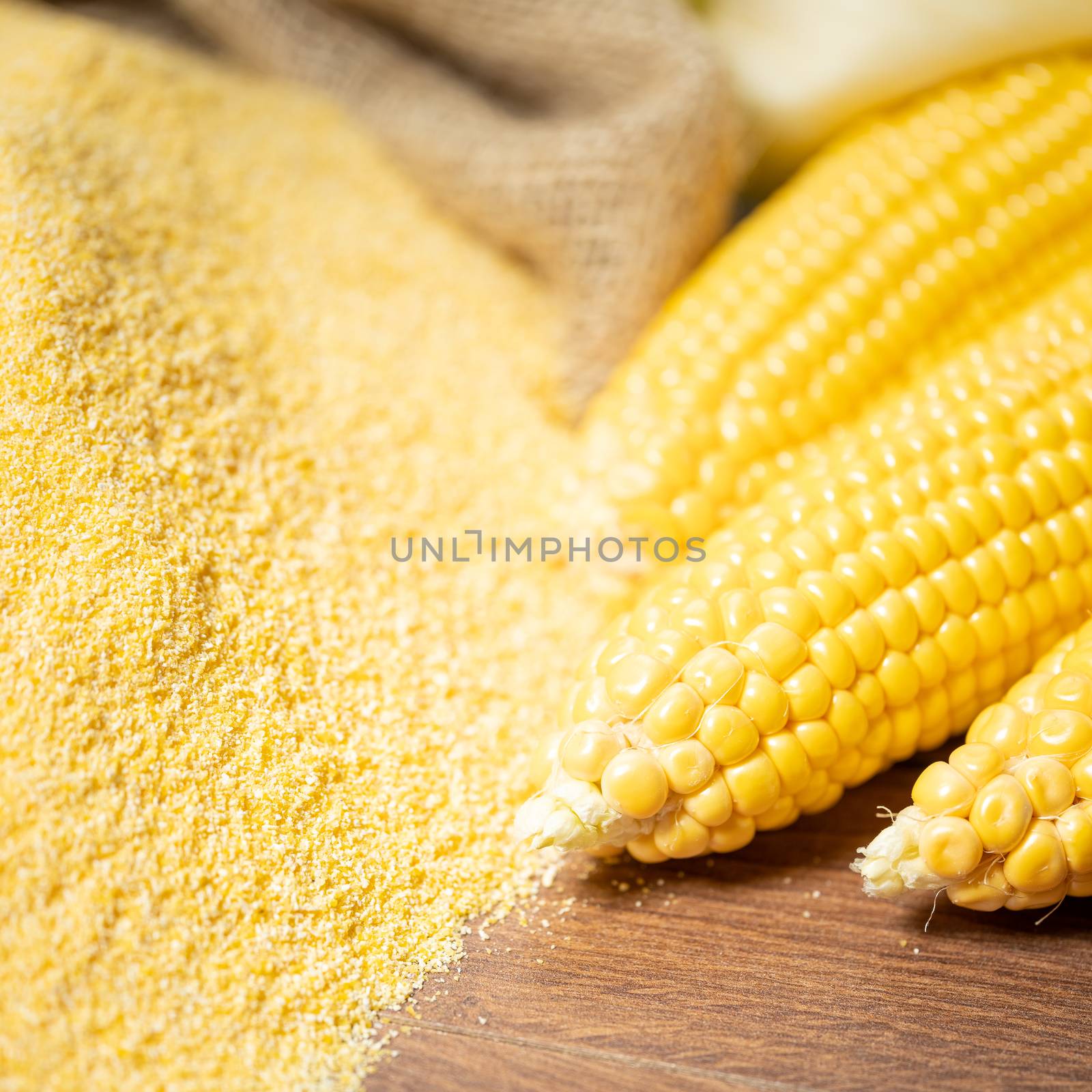 Ripe young sweet corn cob,on stack cornmeal on wooden background,close up.Gluten free food concept