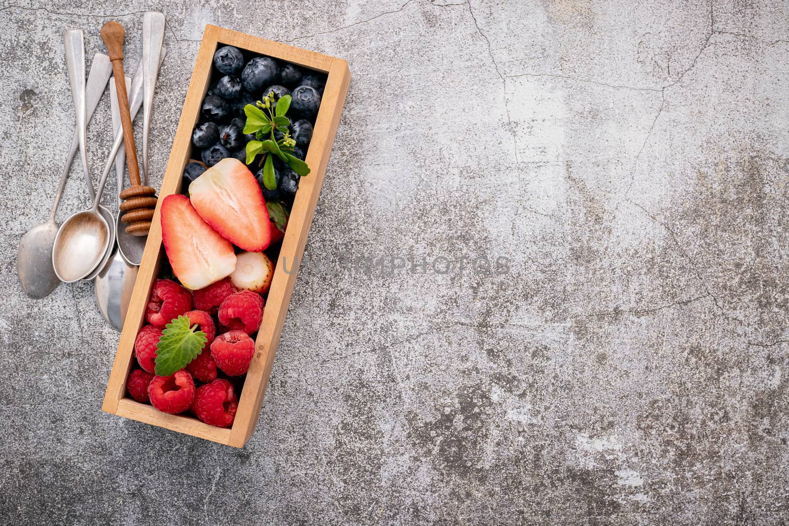 Various fresh berries blueberry, raspberry and strawberry in wooden box setup on concrete background .