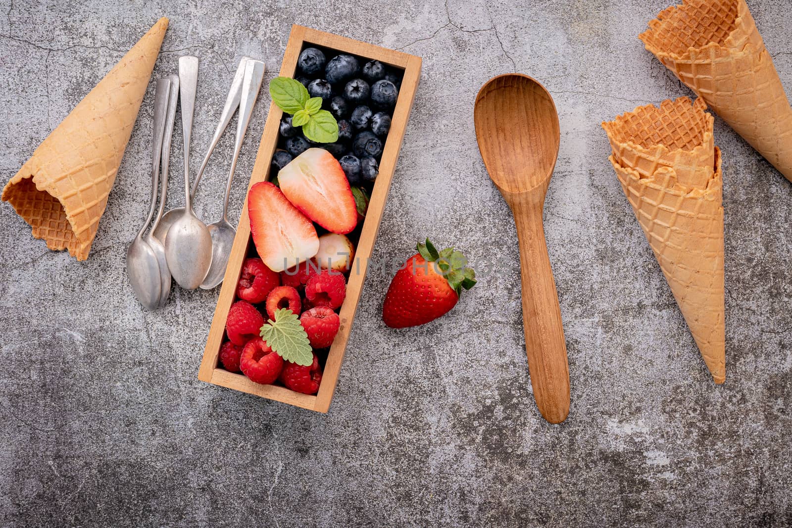 Waffle cones with berries in wooden box setup on concrete backgr by kerdkanno