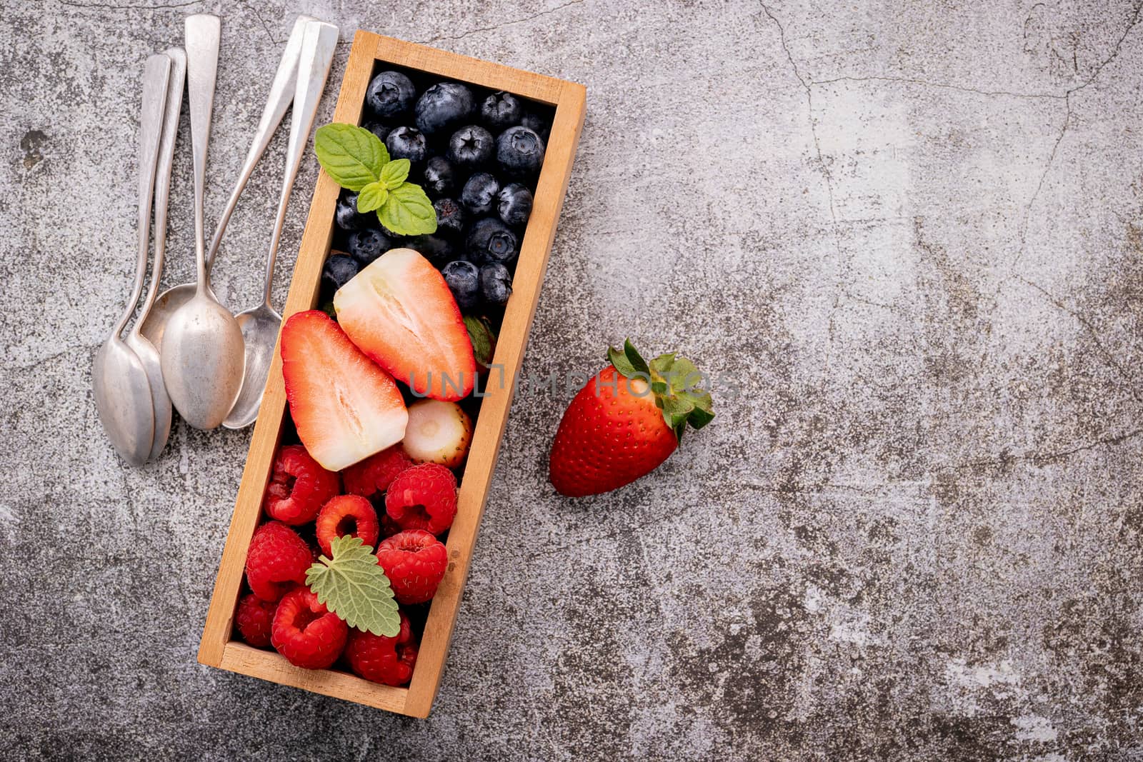 Various fresh berries blueberry, raspberry and strawberry in wooden box setup on concrete background .