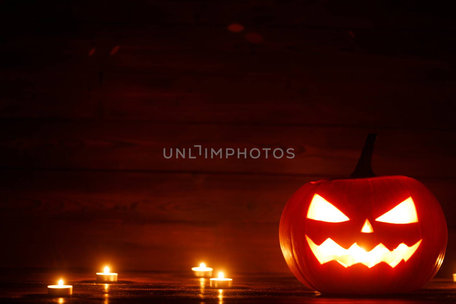 Halloween Jack o Lantern pumpkin head and burning candles on wooden background