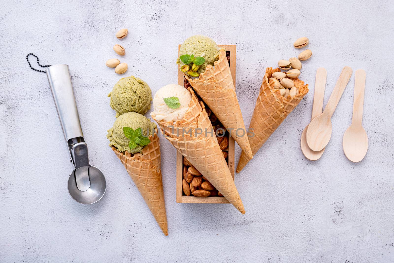 Pistachio and vanila ice cream in cones  with mixed nut setup on white stone background . Summer and Sweet menu concept.