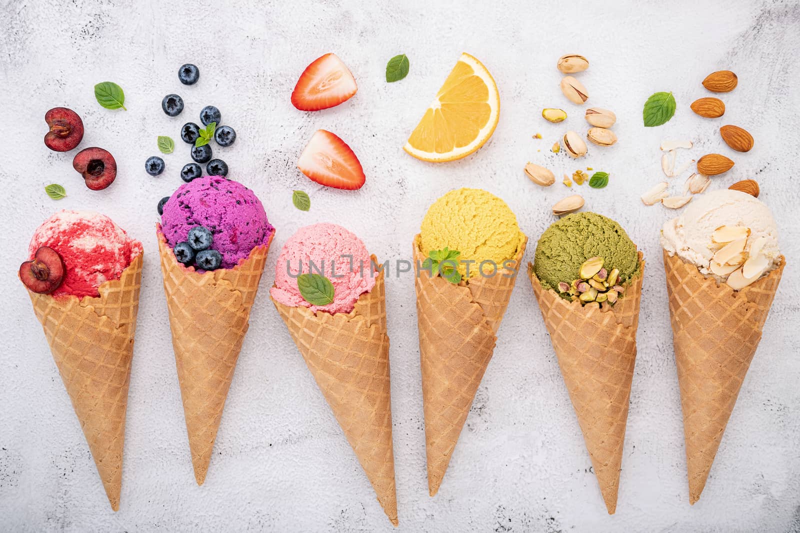 Various of ice cream flavor in cones blueberry ,pistachio ,almond ,orange and cherry setup on white stone background . Summer and Sweet menu concept.