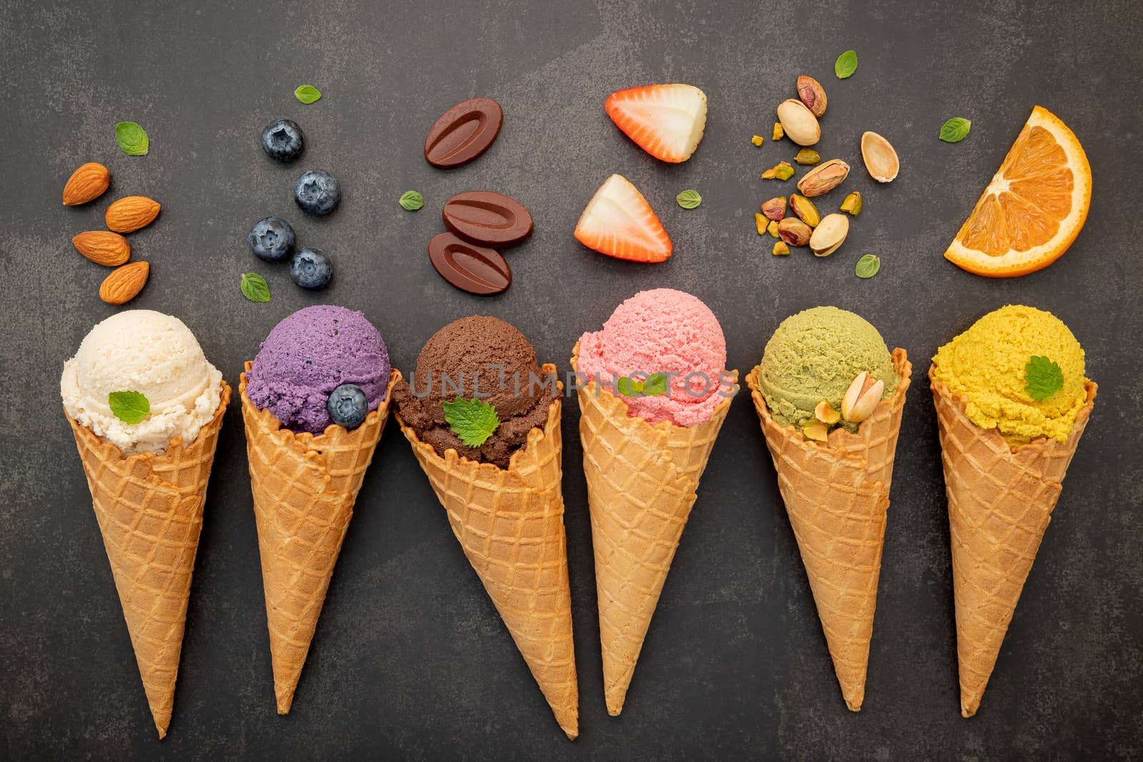 Various of ice cream flavor in cones blueberry ,pistachio ,almond ,orange and chocolate setup on dark stone background . Summer and Sweet menu concept.