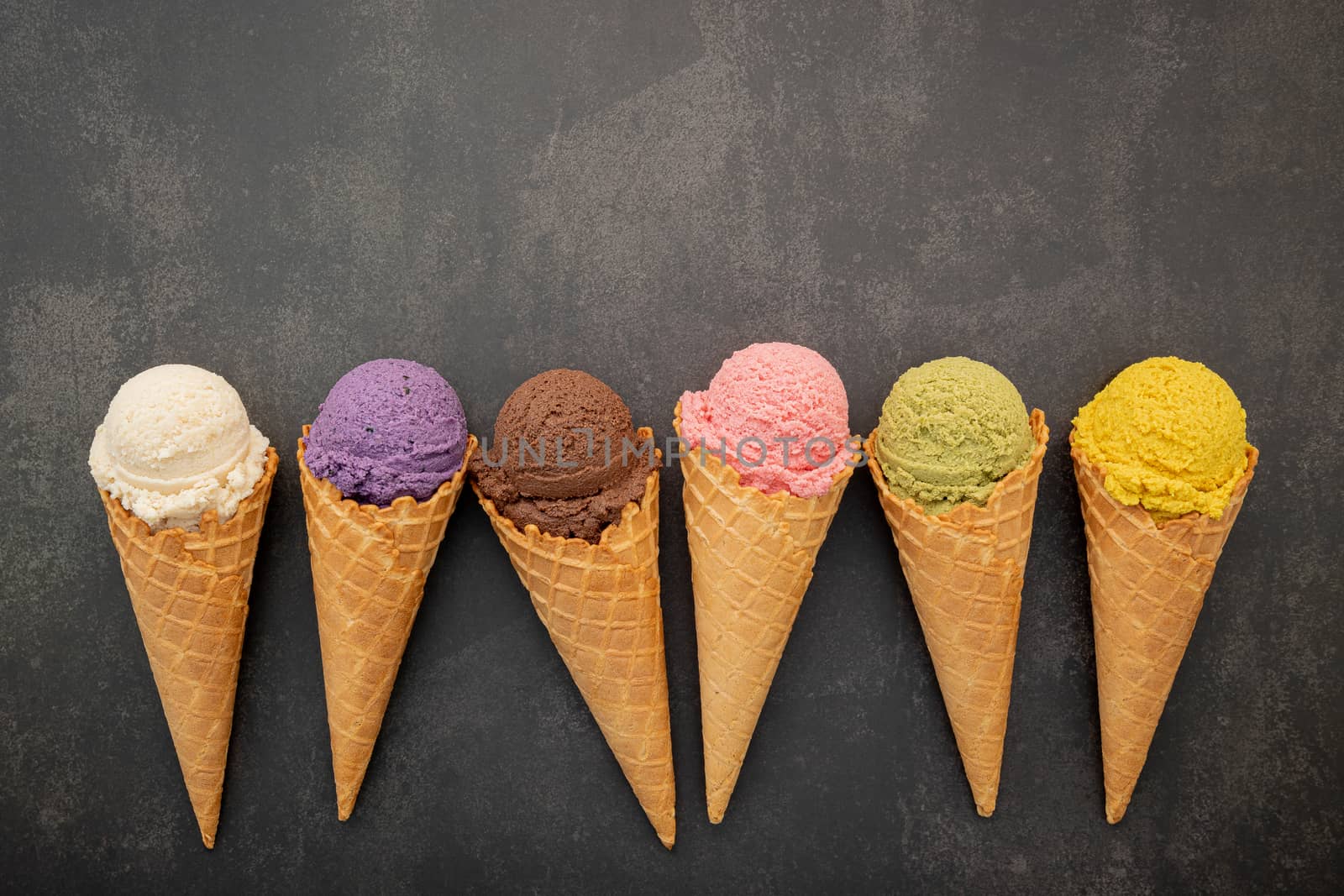 Various of ice cream flavor in cones blueberry ,pistachio ,almond ,orange and chocolate setup on dark stone background . Summer and Sweet menu concept.