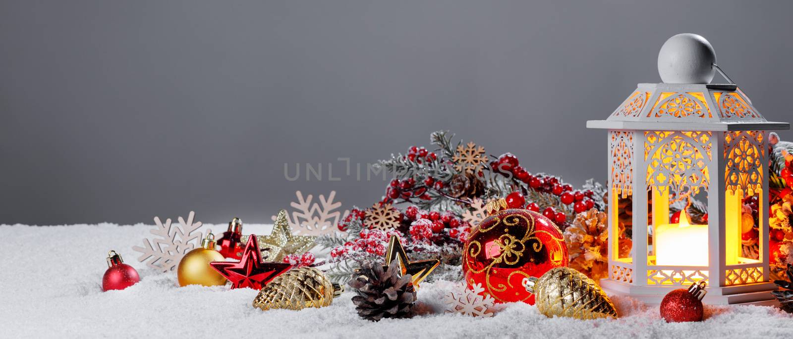 Glowing Christmas lantern and decor of fir tree branches and baubles in snow