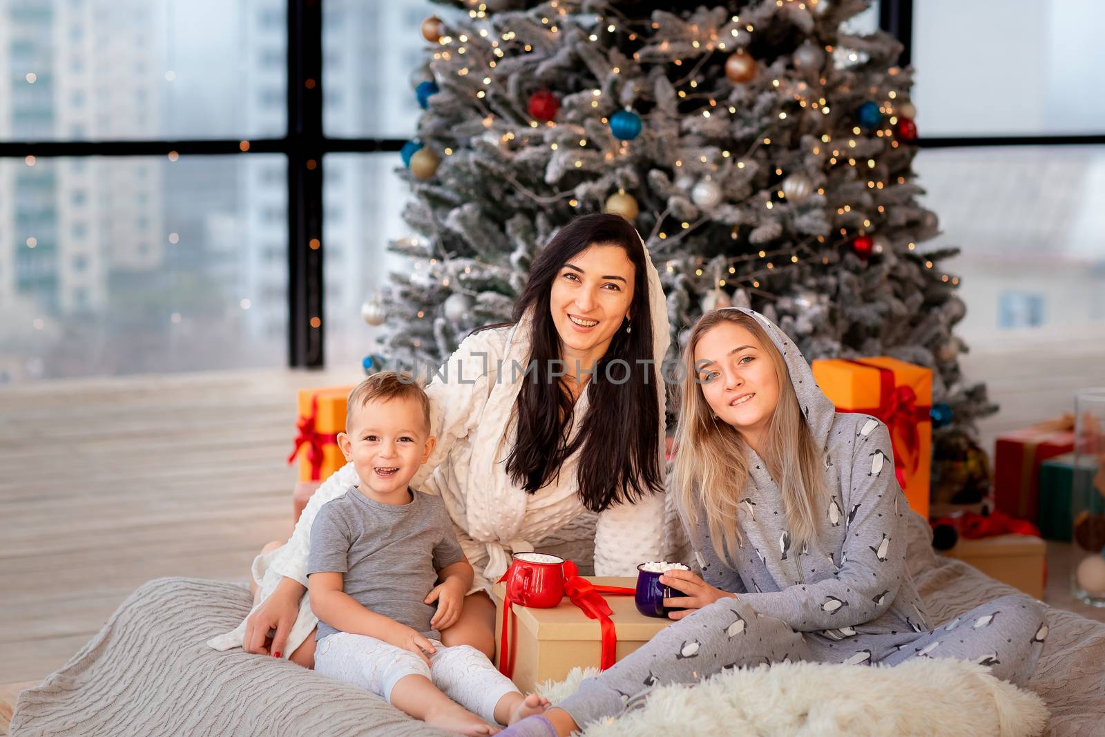Happy cheerful family near Christmas tree. Mother and kids wearing pajama having fun near tree in the morning. Merry Christmas and Happy Holidays concept