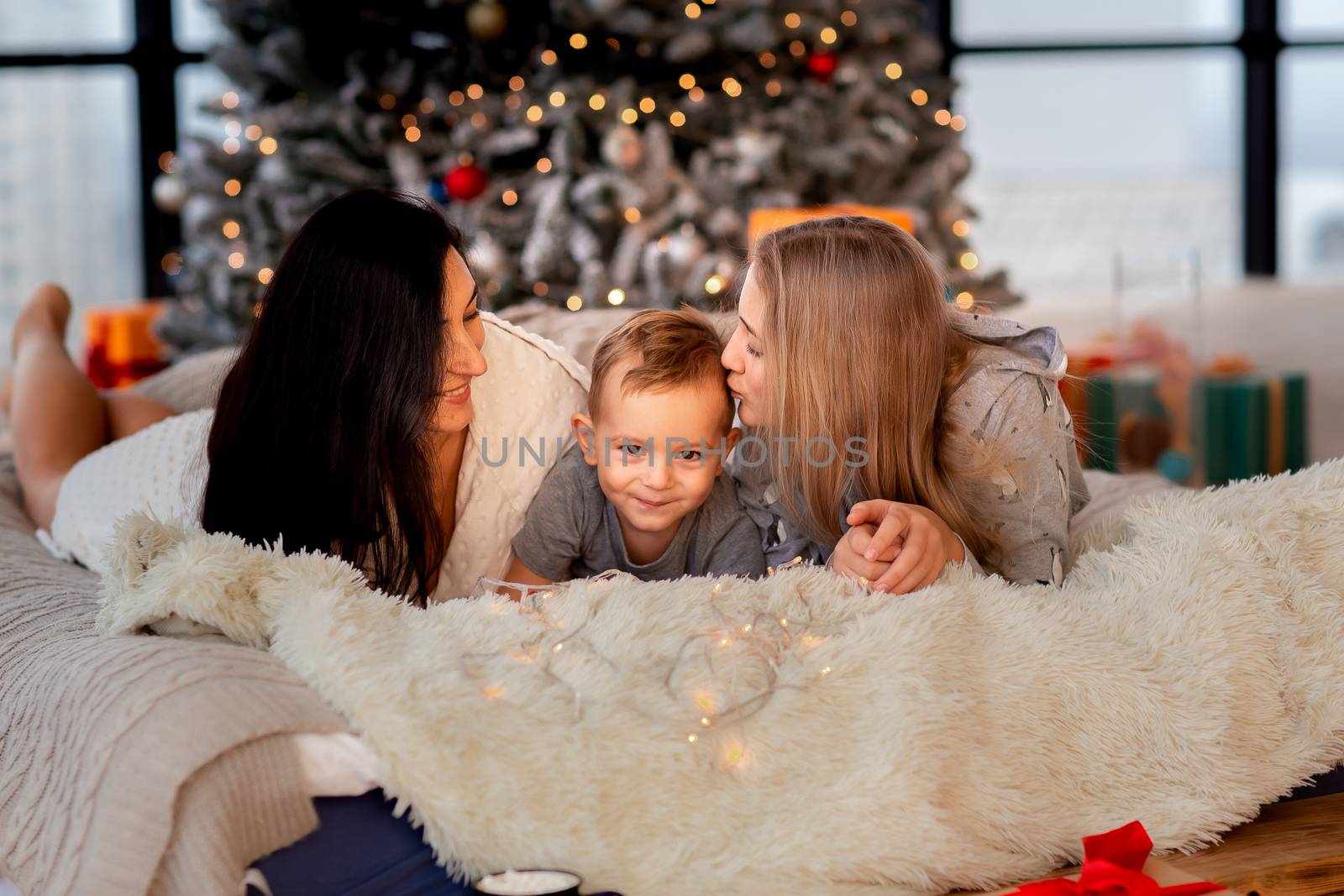 Happy cheerful family near Christmas tree. Mother and kids wearing pajama having fun near tree in the morning. Merry Christmas and Happy Holidays concept